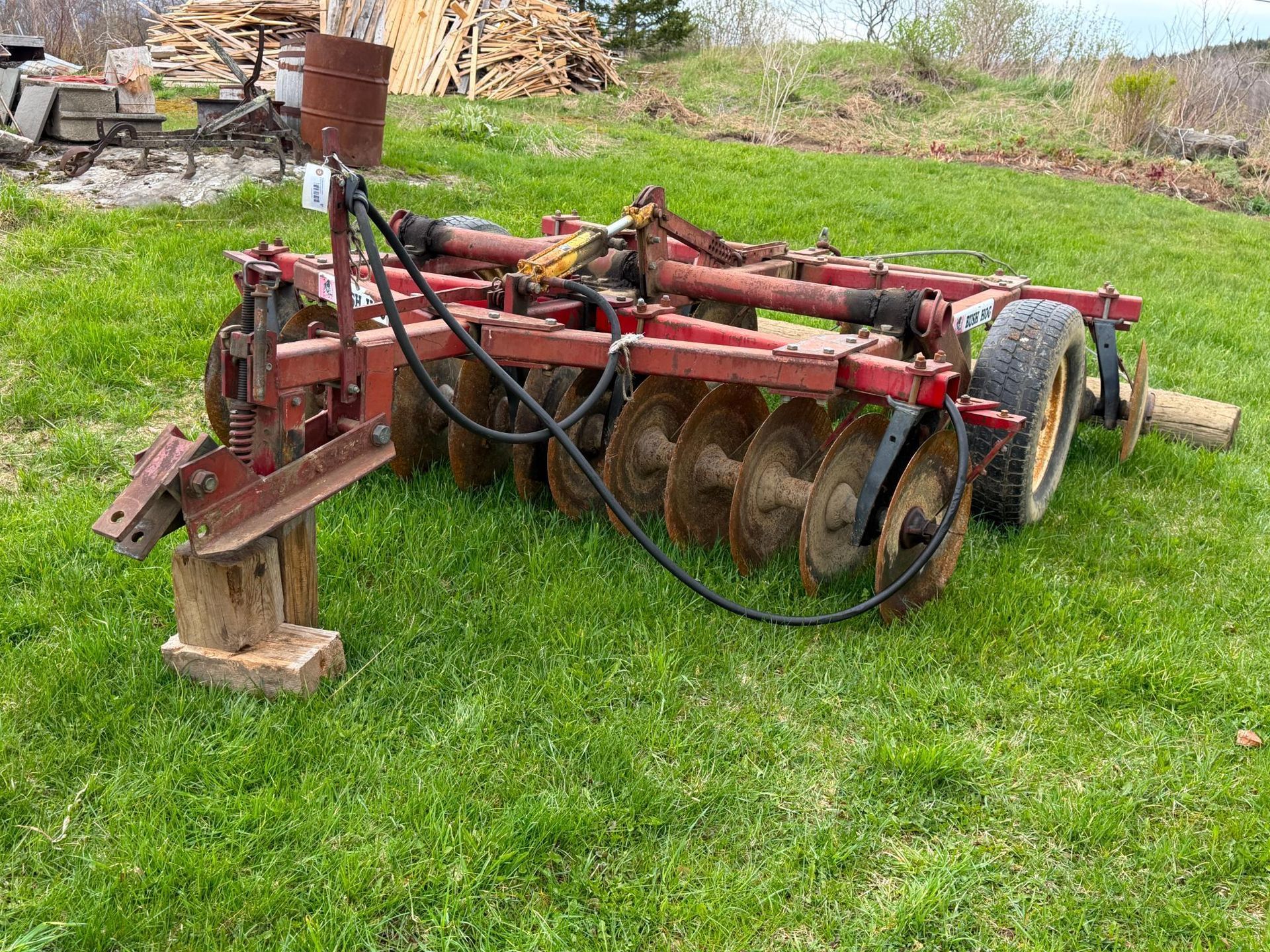 Red farm tillage implement with disc blades and hoses sitting on grass in a rural yard