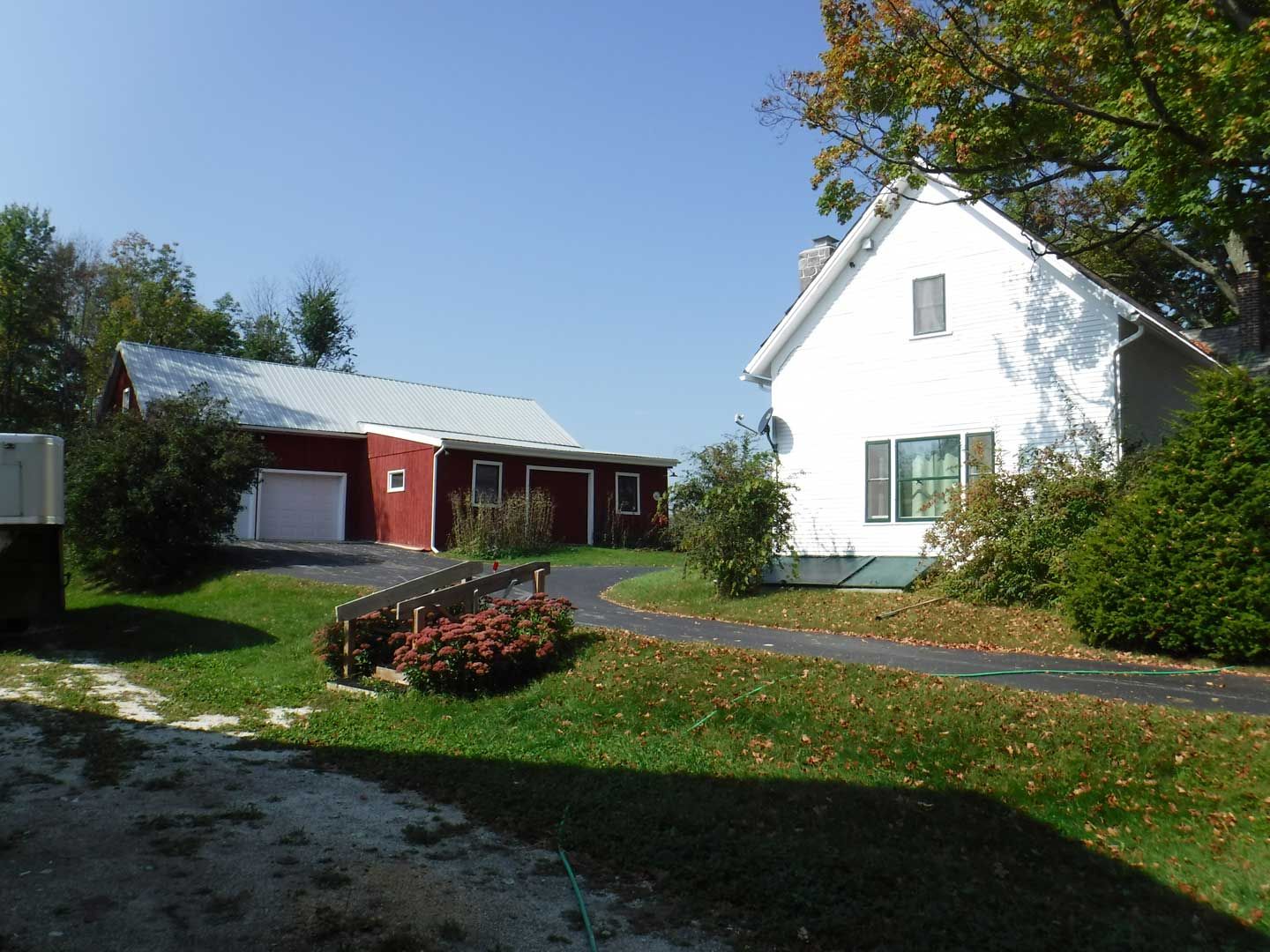 White house and red barn with driveway and green lawn under a blue sky.