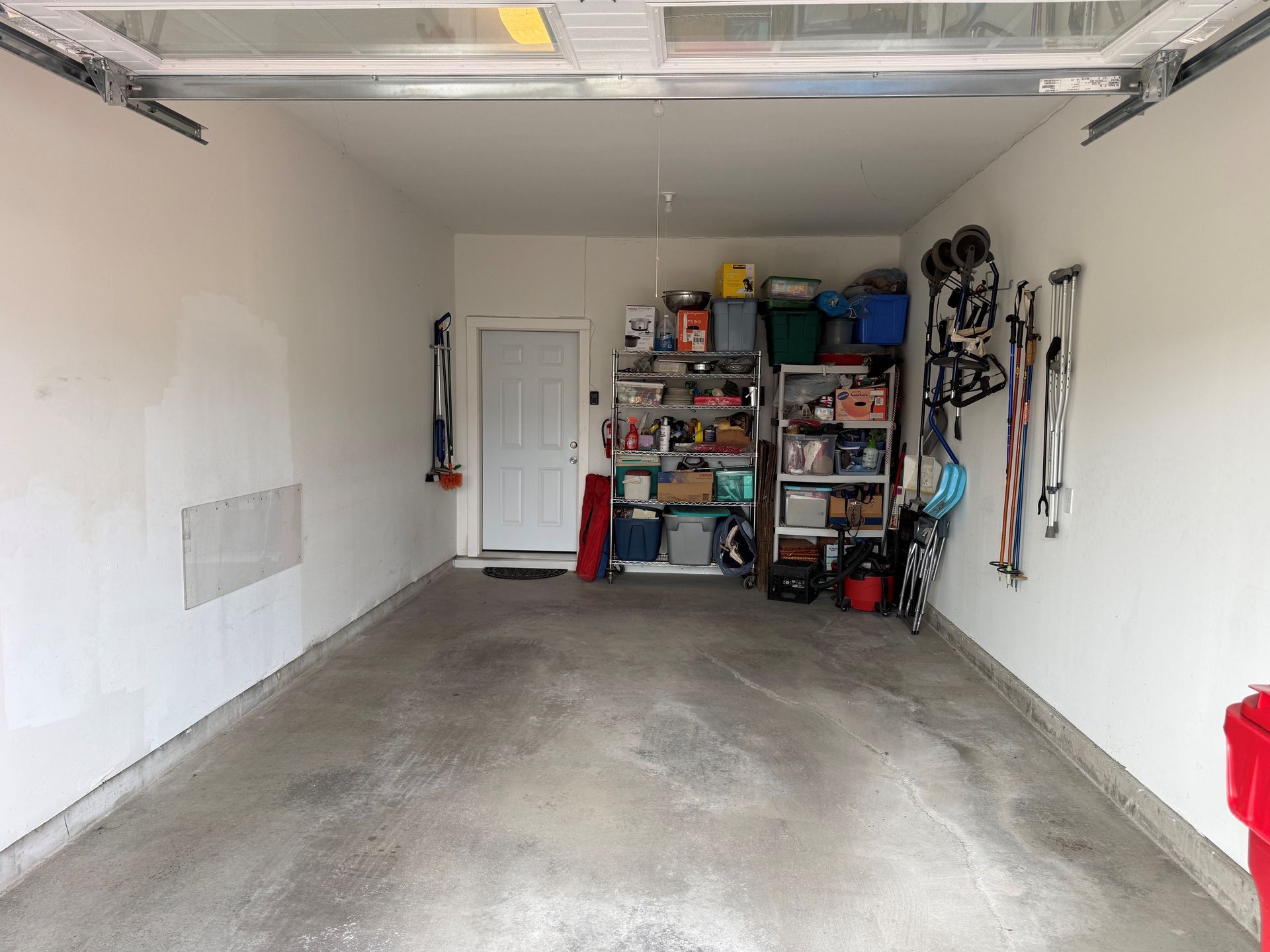 Empty garage with concrete floor, white walls, and storage shelves at the back.