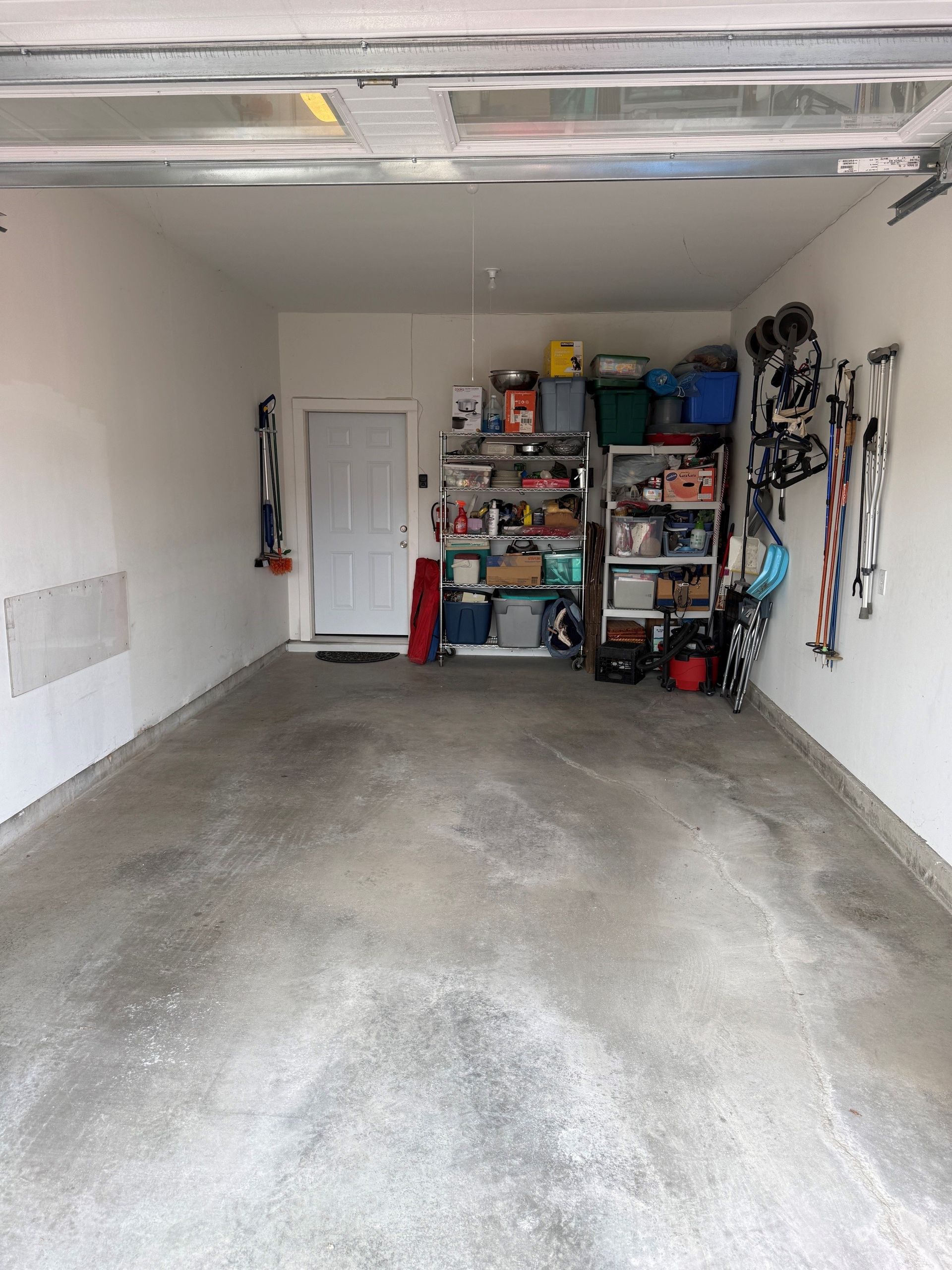 Empty garage with concrete floor, white walls, and shelves of tools and storage at the back.