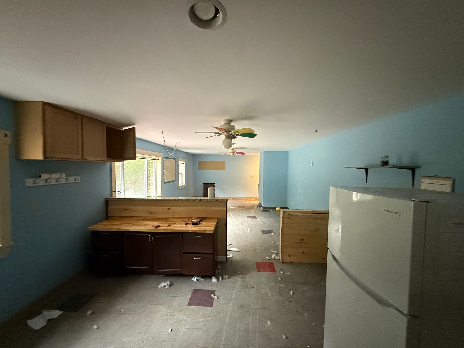 Empty kitchen with light blue walls, white fridge, wood cabinets
