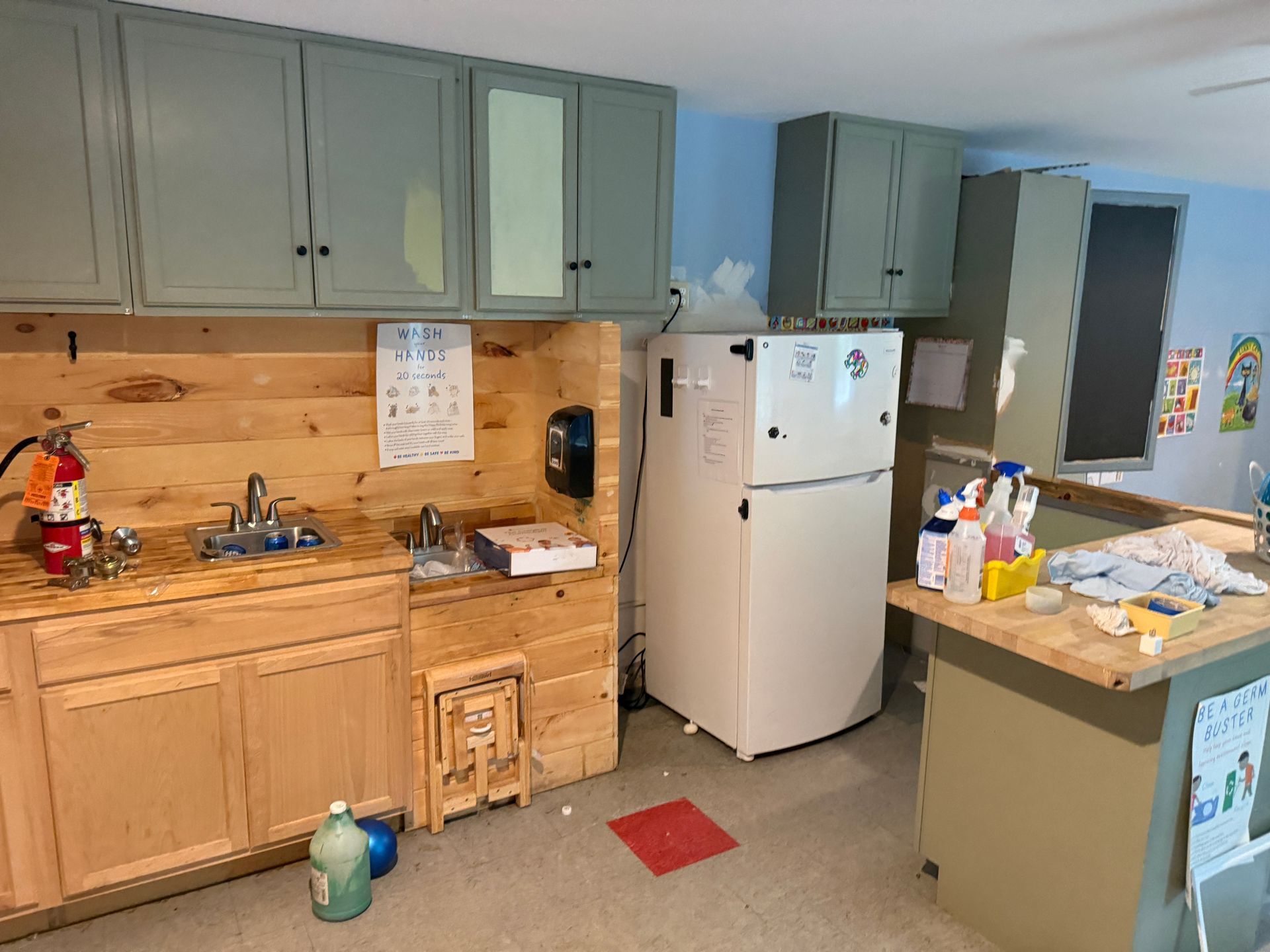 Kitchen with blue-gray cabinets, wooden counters, white fridge, and cleaning supplies on the counter