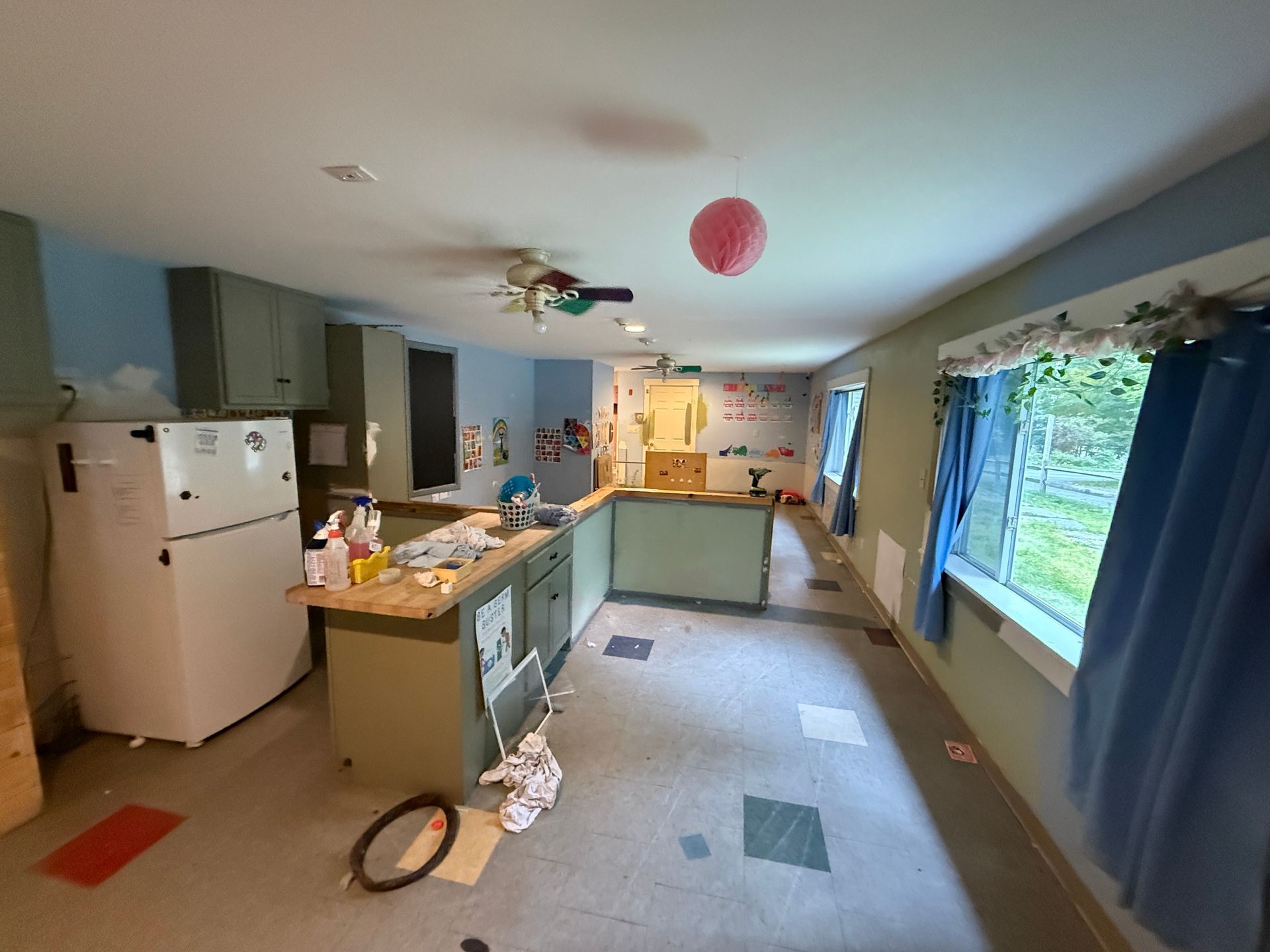 Bright kitchen with teal cabinets, white fridge, and large window by blue curtains.
