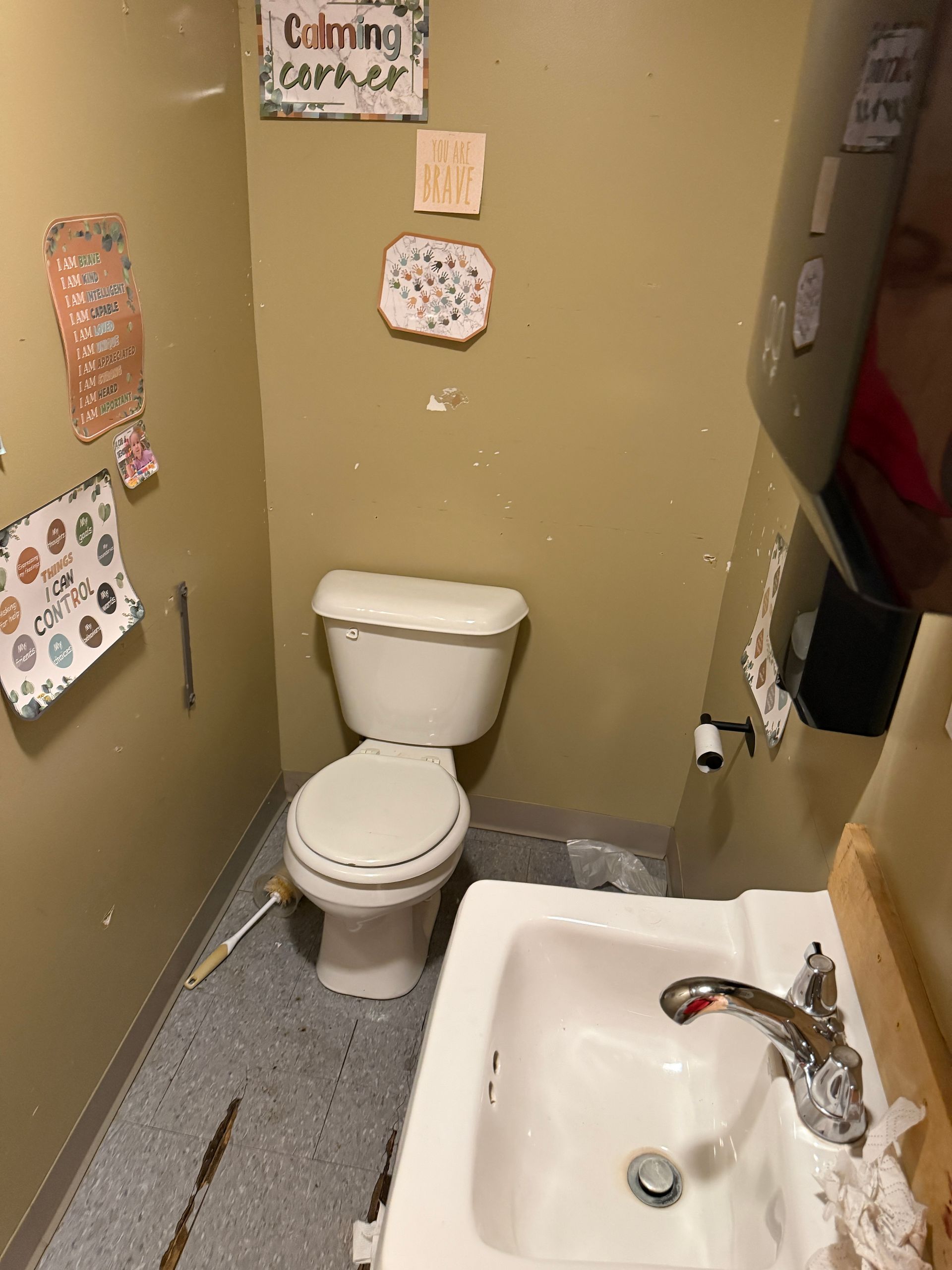 Small bathroom with toilet and sink, tan walls, and children’s drawings taped up.