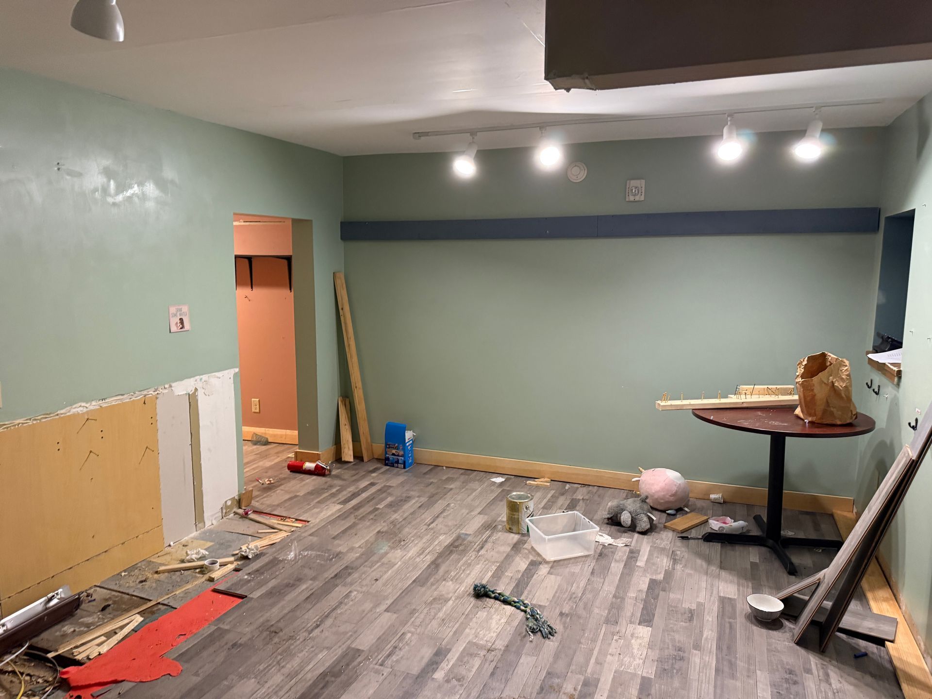 Partially renovated room with green walls, scattered tools, and a work table under ceiling lights