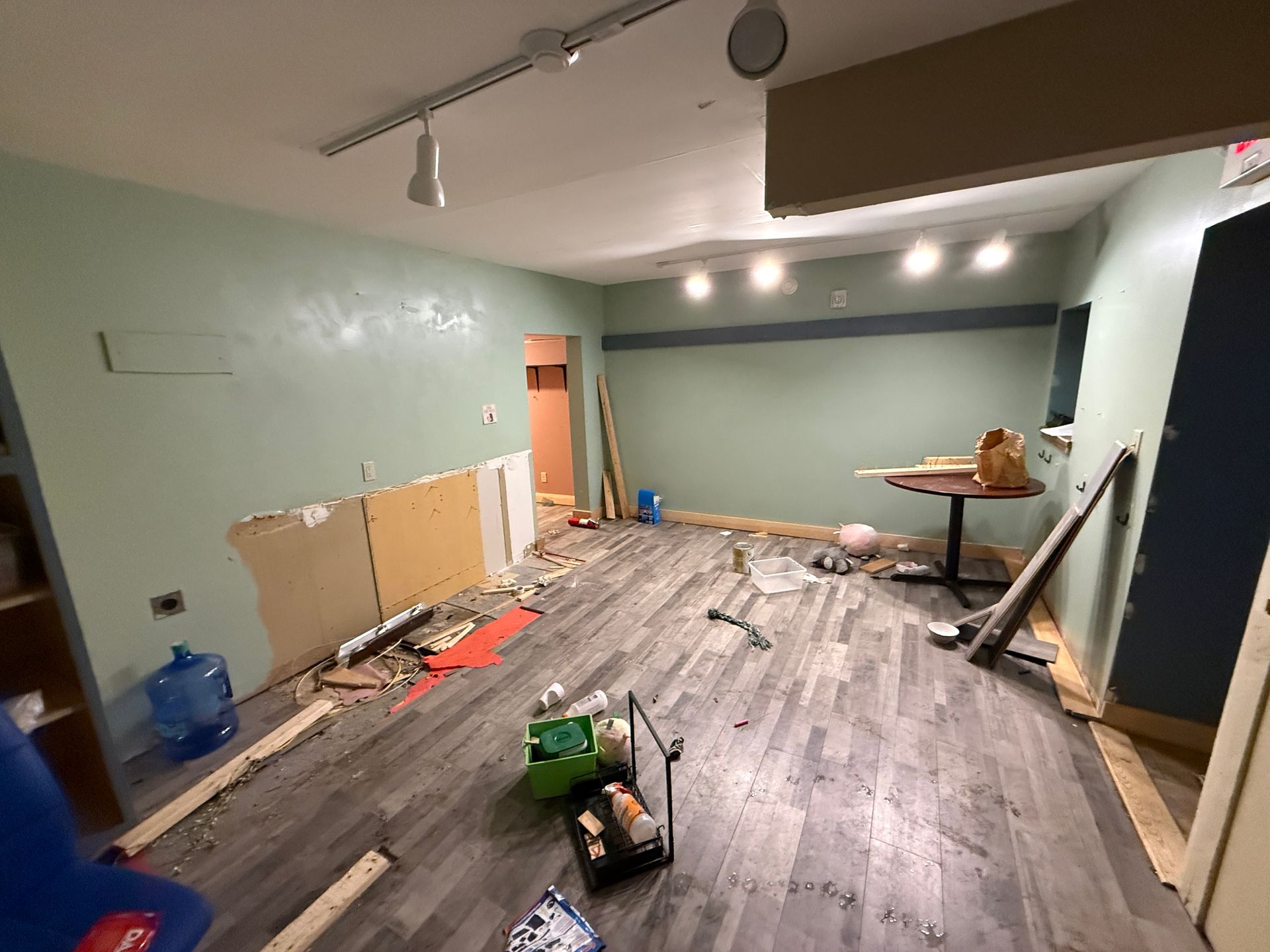 Partially renovated room with wood flooring, scattered tools, cardboard, and construction materials