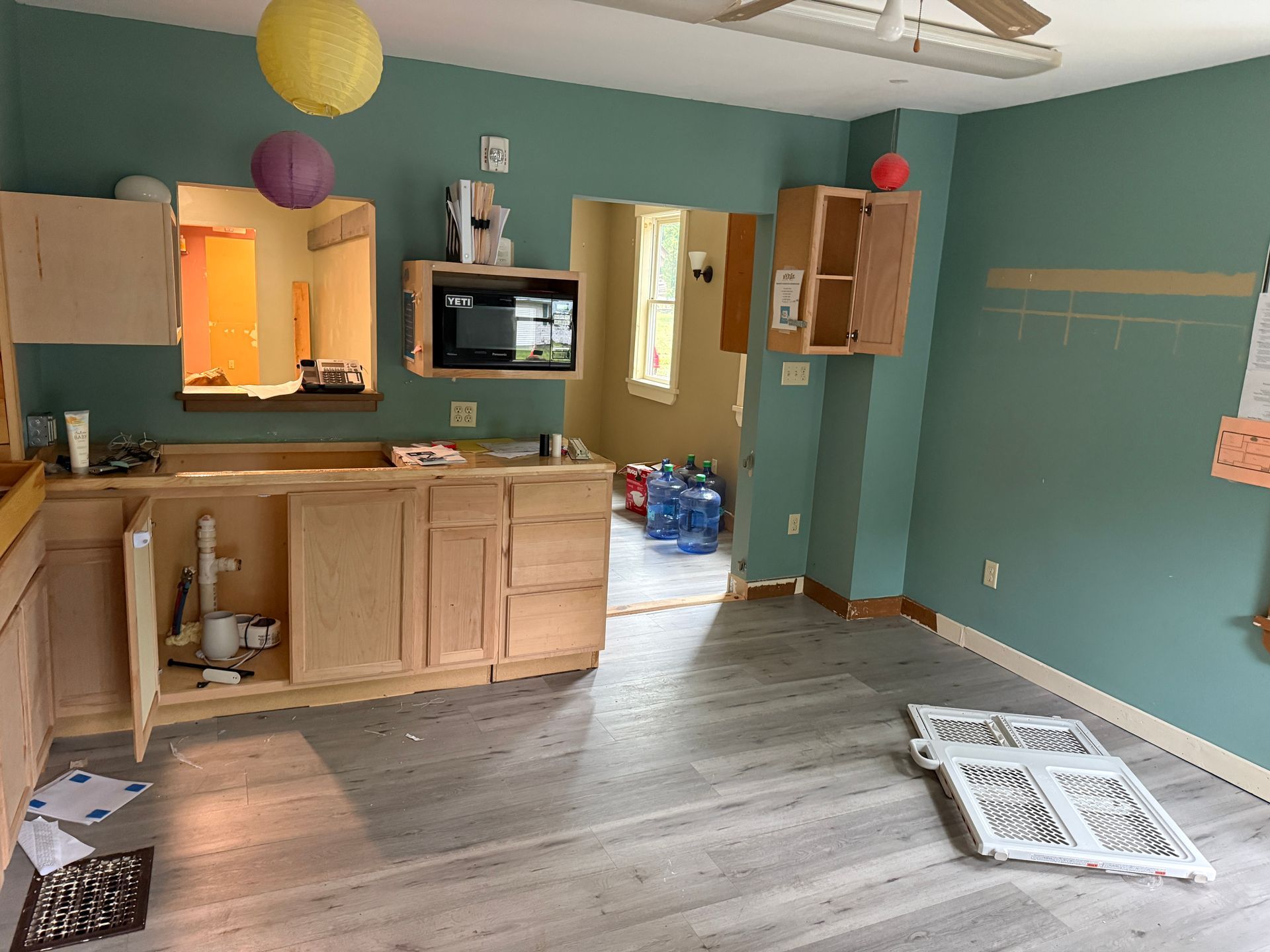 Empty kitchen with light wood cabinets, teal walls, and a doorway to another room.