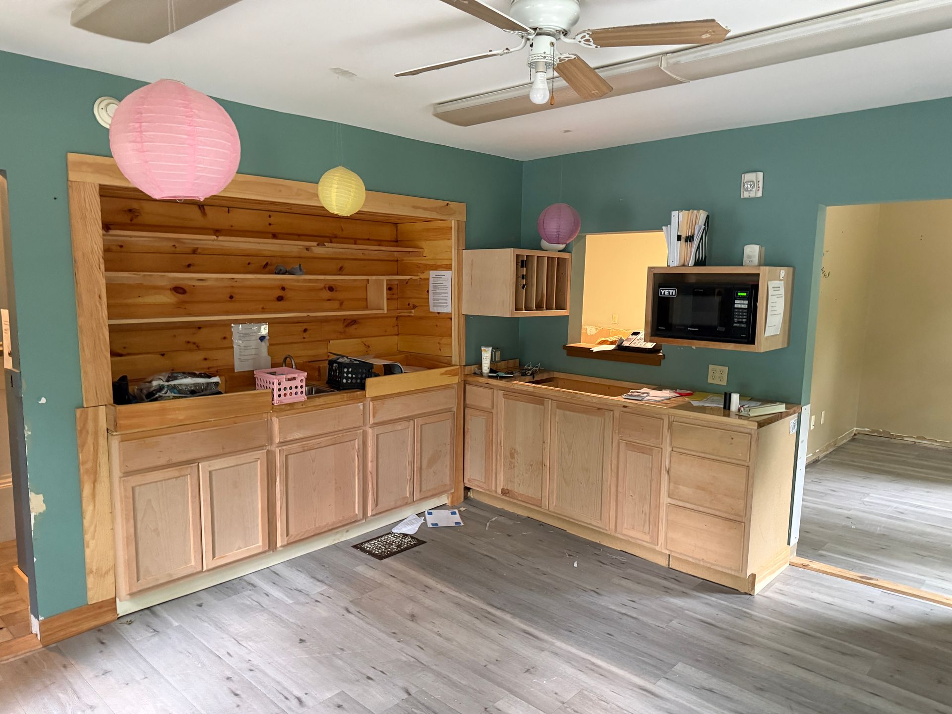 Empty room with wood cabinets, teal walls, hanging paper lanterns, and a microwave on the counter