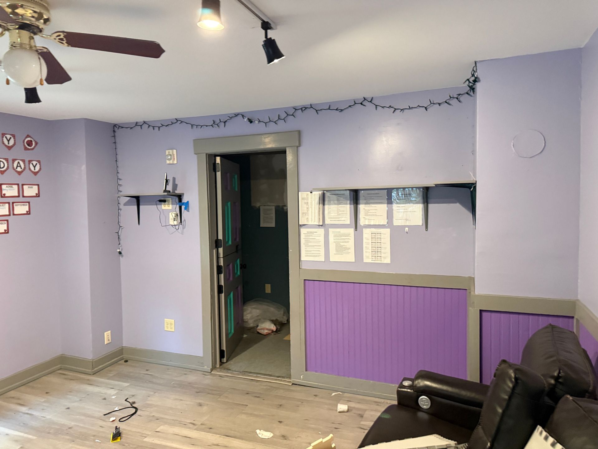 Empty lavender living room with purple wainscoting, open doorway, string lights, and a brown recliner.