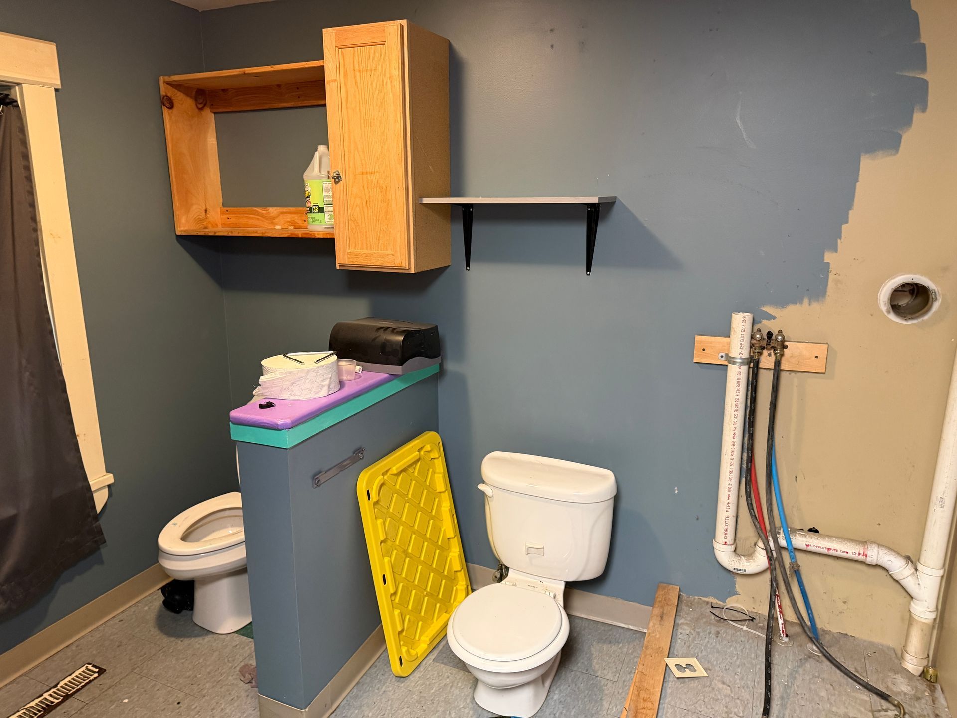 Small unfinished bathroom with toilet, sink, wooden cabinet, exposed plumbing