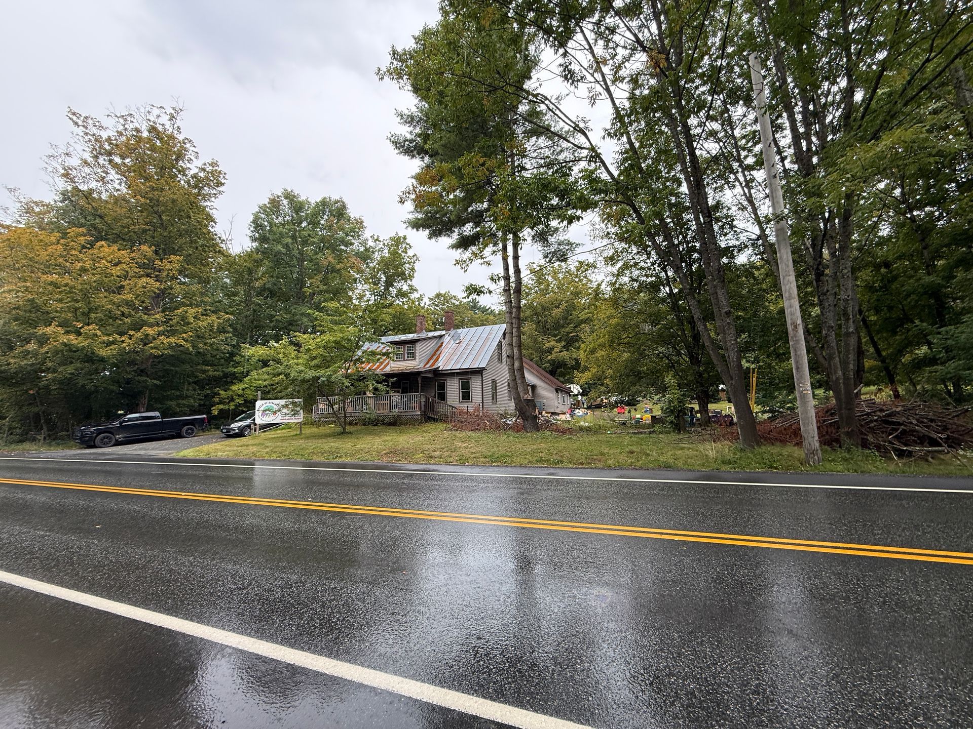 Rainy roadside with a small house and trees beside a wet two-lane road