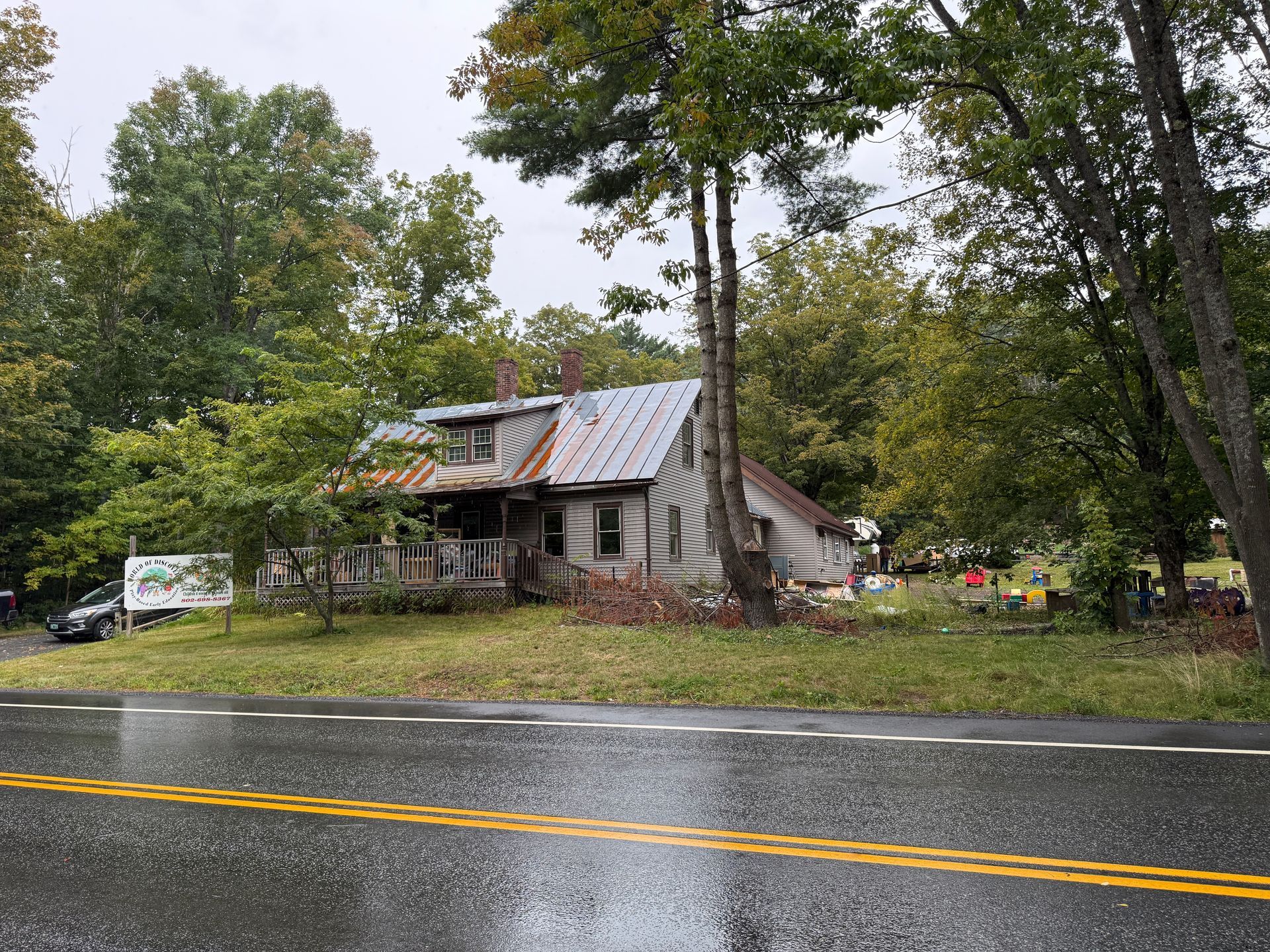 Small house by a wet roadside, surrounded by trees under an overcast sky.