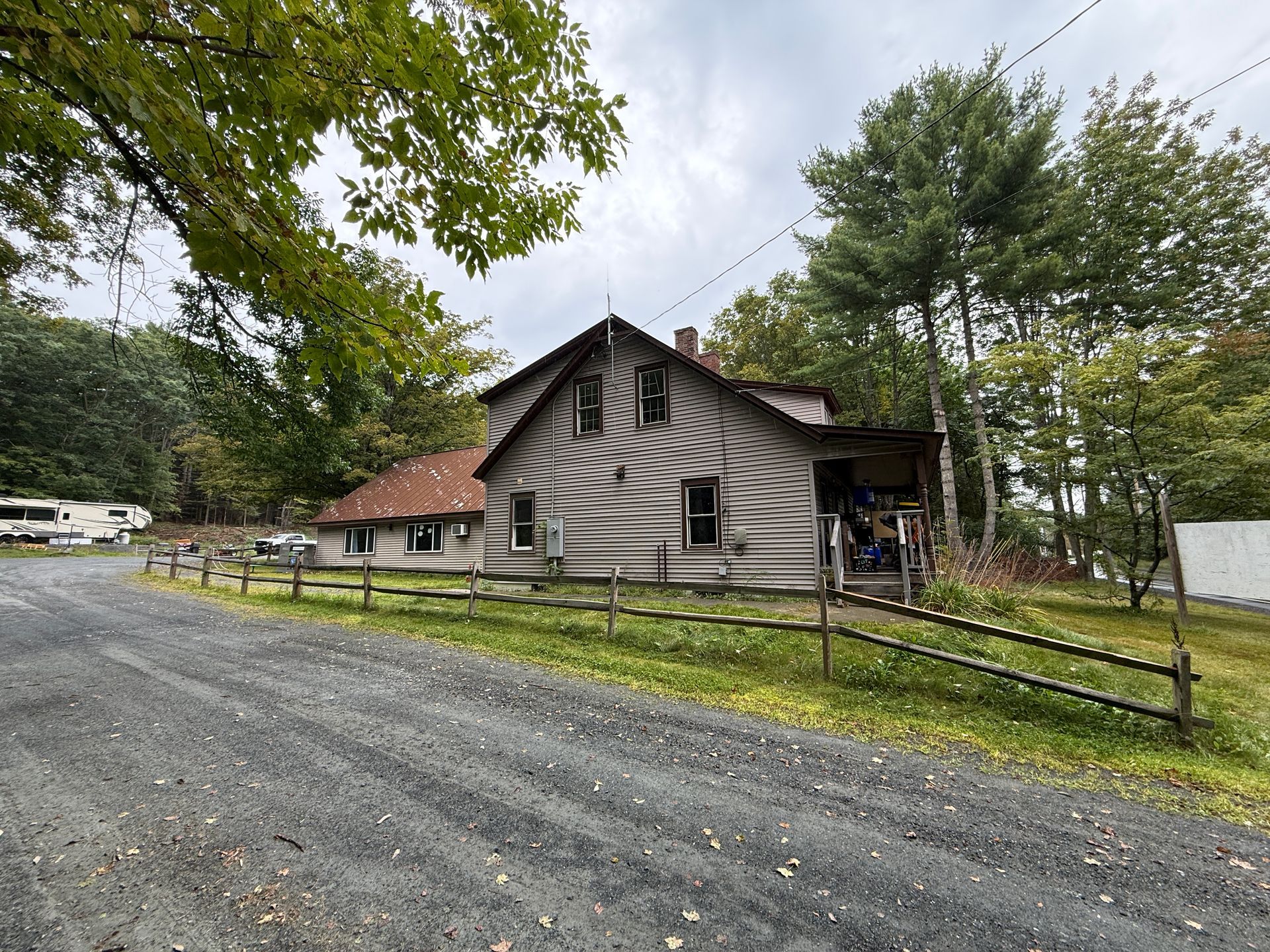 Gravel driveway beside a rustic gray cabin with red roof, trees, and a fence in a wooded setting
