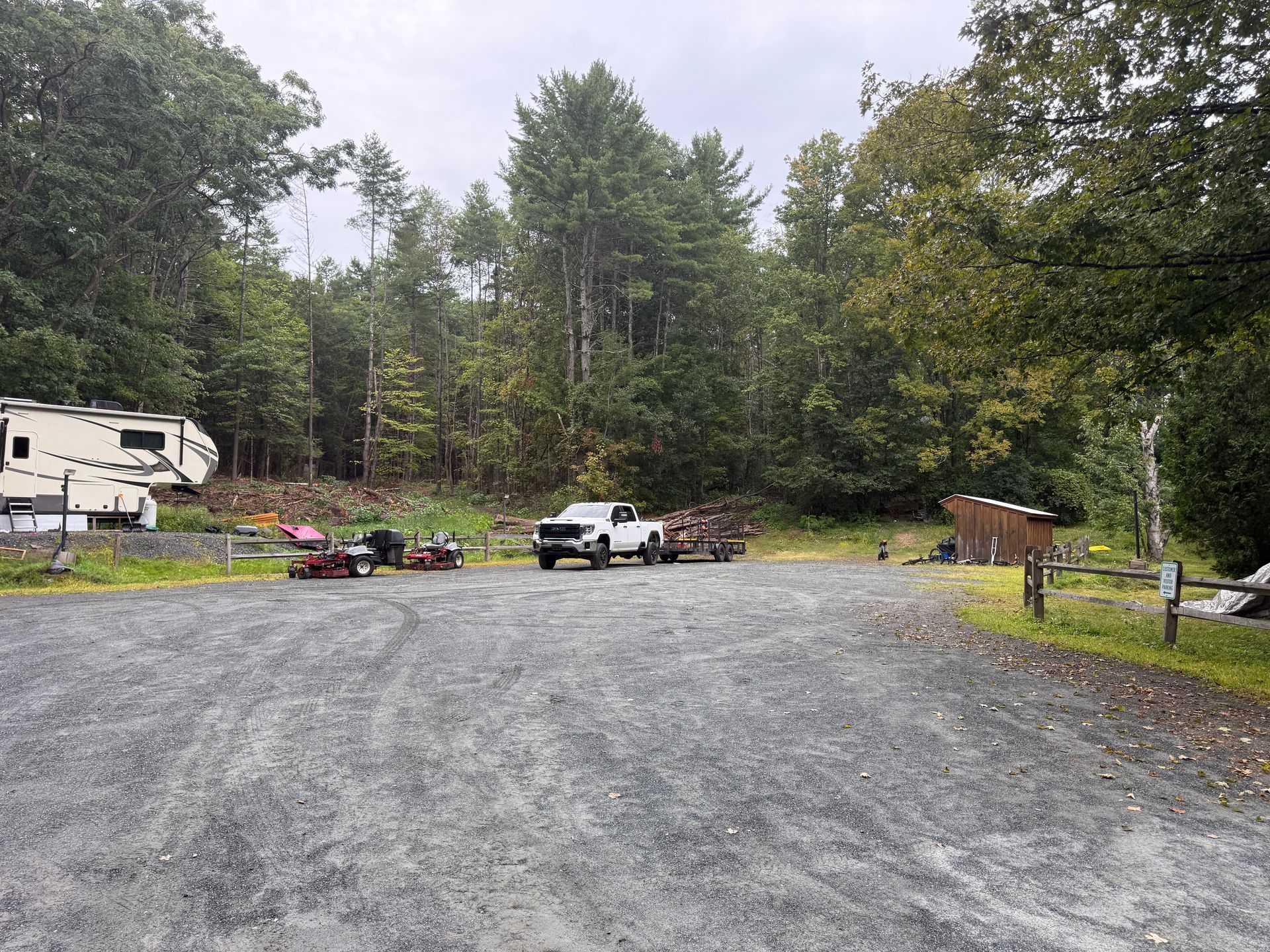 Gravel campsite with a white truck, RV, picnic table, and wooded trees on a cloudy day
