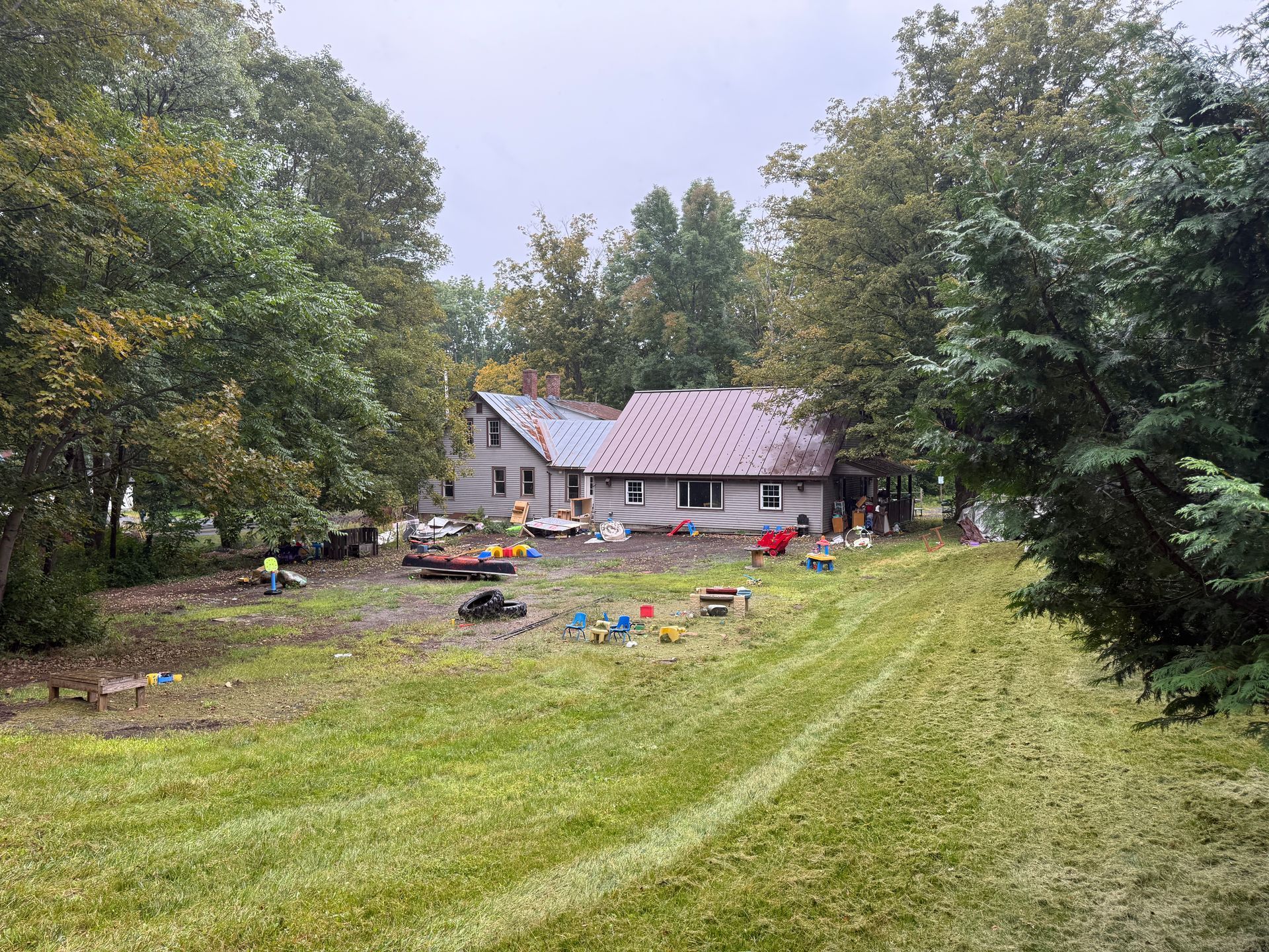Rural yard with a small house, and trees under an overcast sky