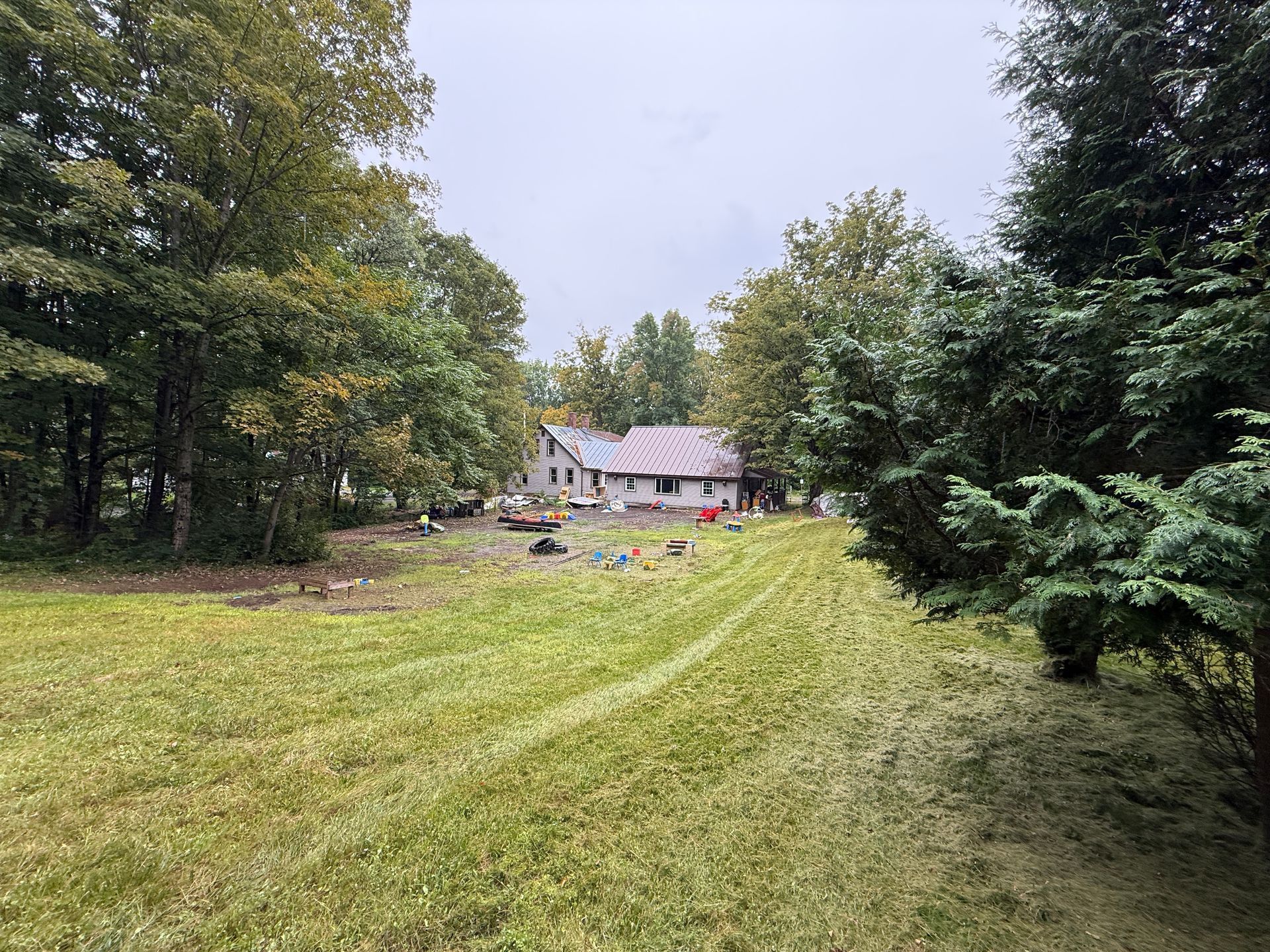 Grassy path leading to a small house surrounded by trees under an overcast sky