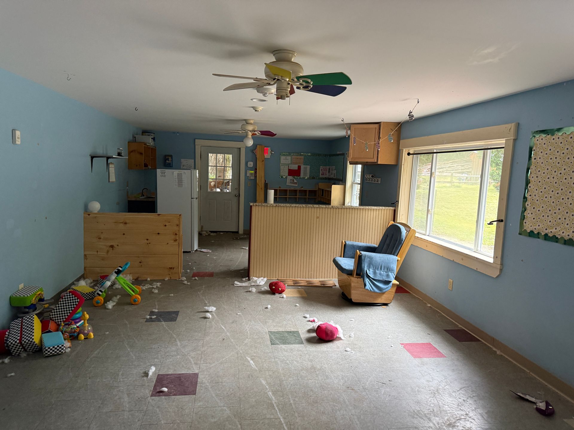 living room with blue walls, toys on the floor, a recliner, and a ceiling fan near large windows.