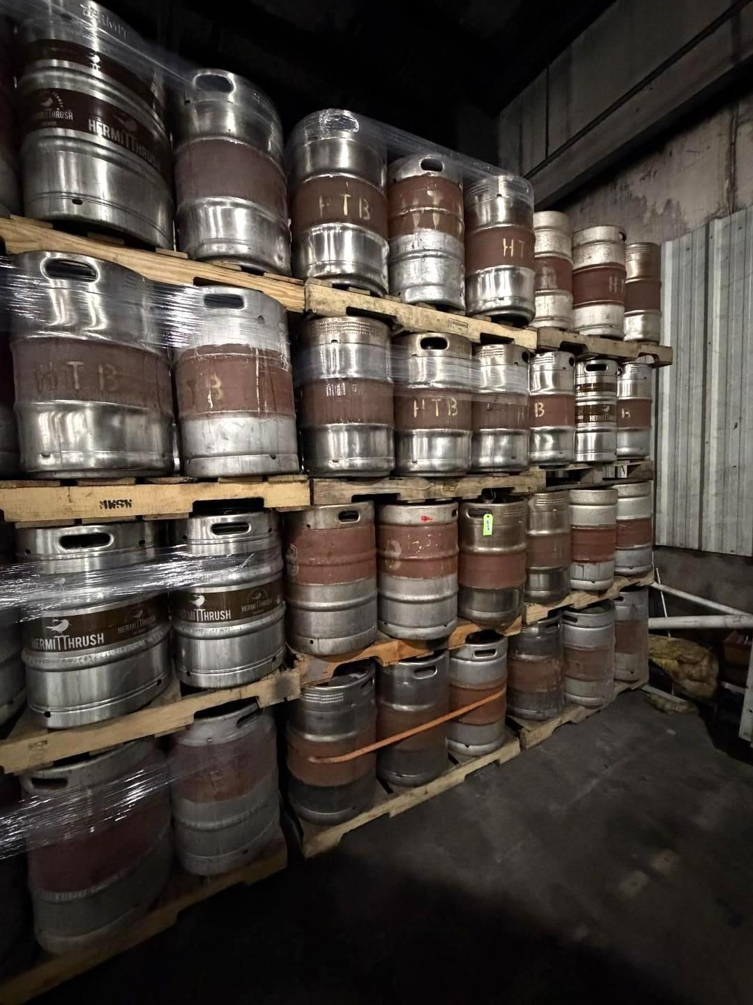 Stacks of beer kegs stored on wooden pallets in a dim warehouse aisle