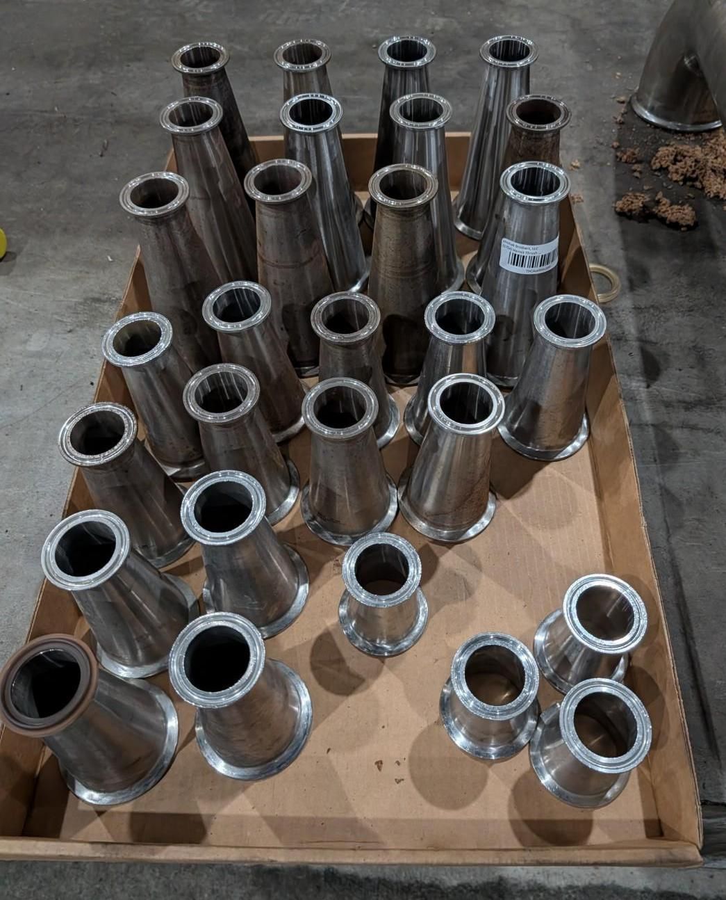 Metal pipe fittings arranged on a cardboard sheet in a workshop setting.