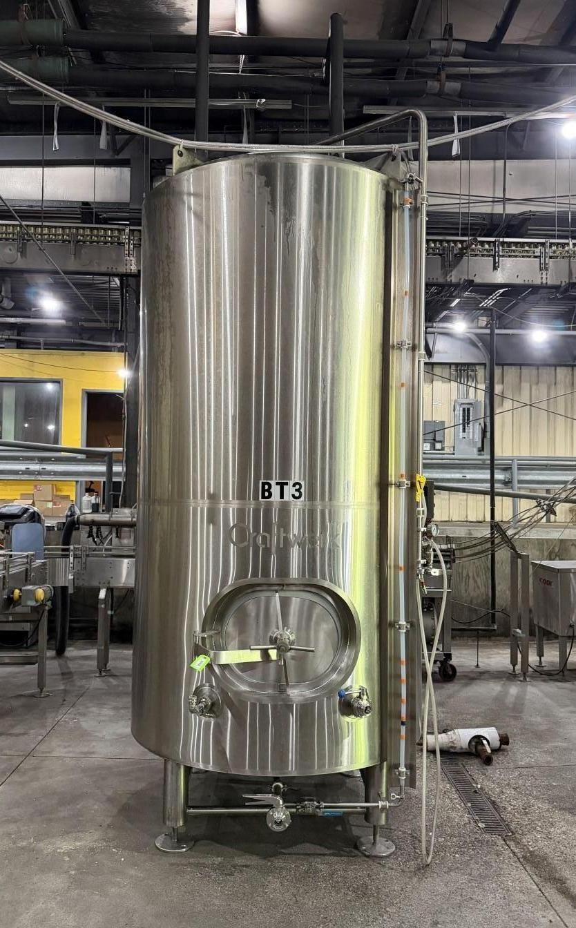 Large stainless-steel industrial tank in a factory with pipes and equipment around it