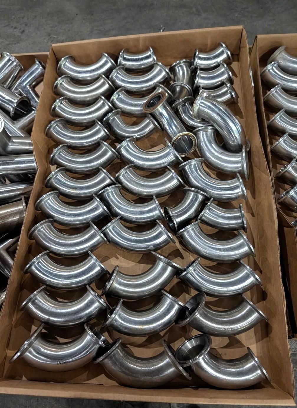 Cardboard boxes filled with shiny metal elbow pipe fittings piled together