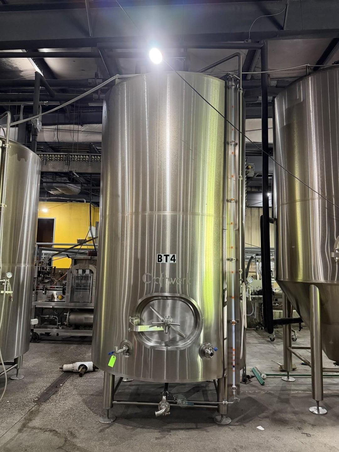 Large stainless steel industrial tank in a factory, with pipes and equipment around it.