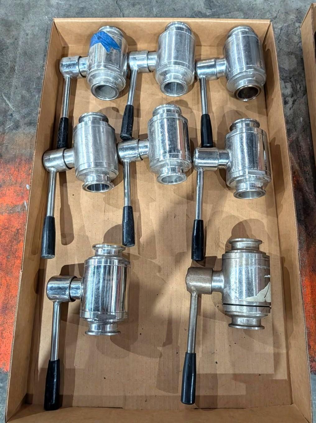 Open cardboard box containing seven chrome hydraulic valves with black levers and blue caps