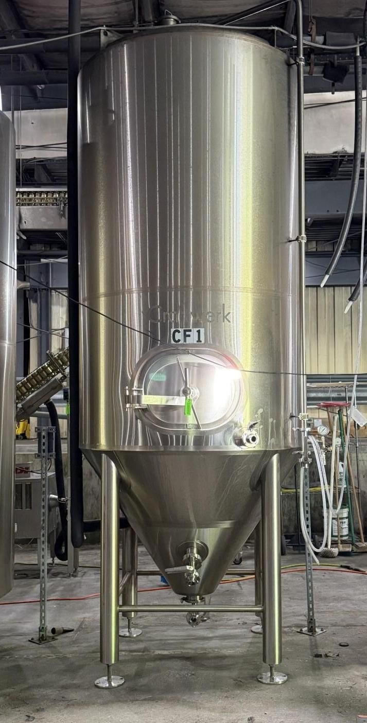 Large stainless steel industrial tank with conical bottom in a factory setting