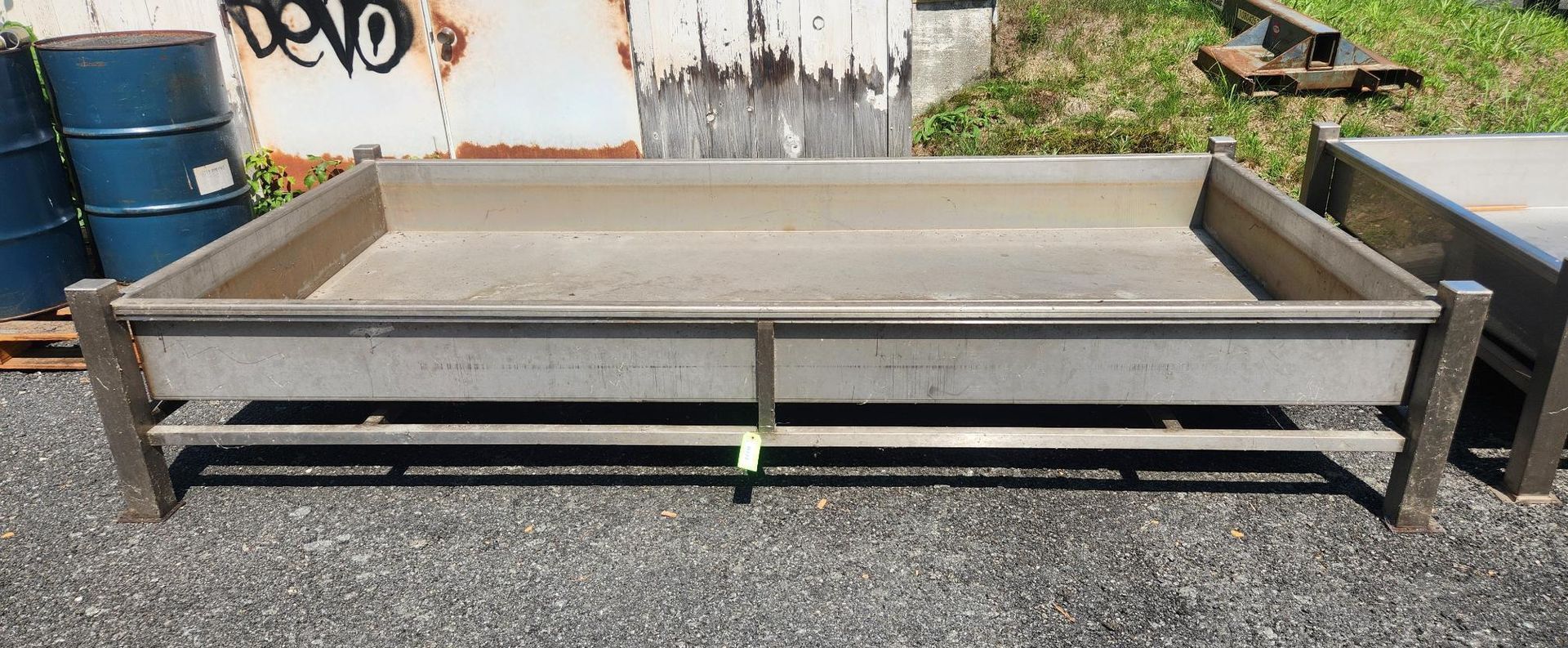 Gray metal platform on gravel with a low front rail and concrete slab top, outdoors near barrels and tools