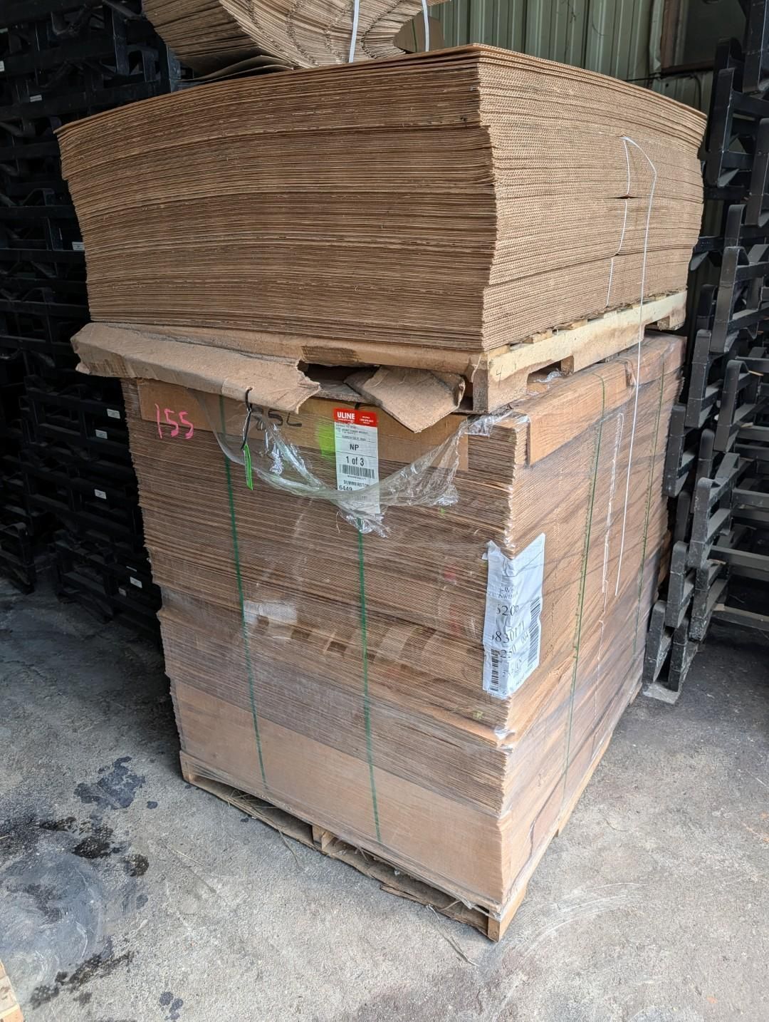 Stacked cardboard on a pallet in a warehouse, wrapped with straps and plastic.