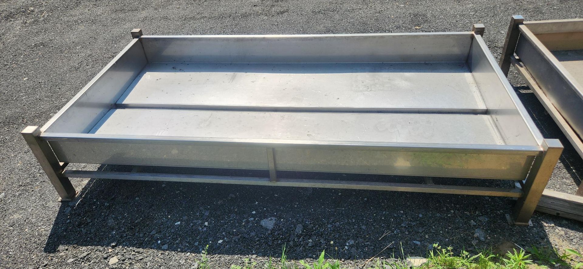 Shallow rectangular metal trough or trailer bed with low sides on asphalt, outdoors.