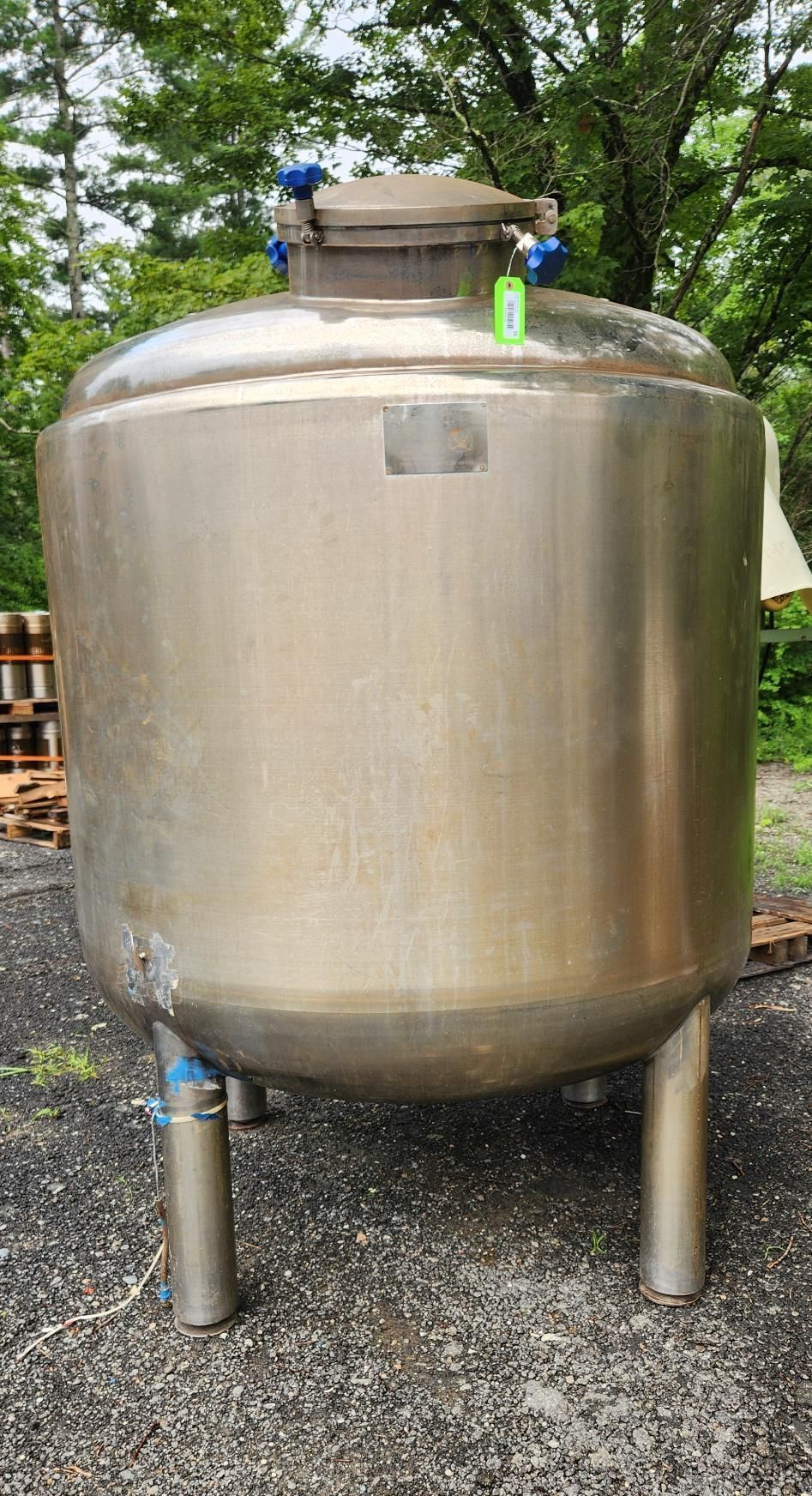 Large stainless steel industrial tank with blue valves standing outdoors on gravel.