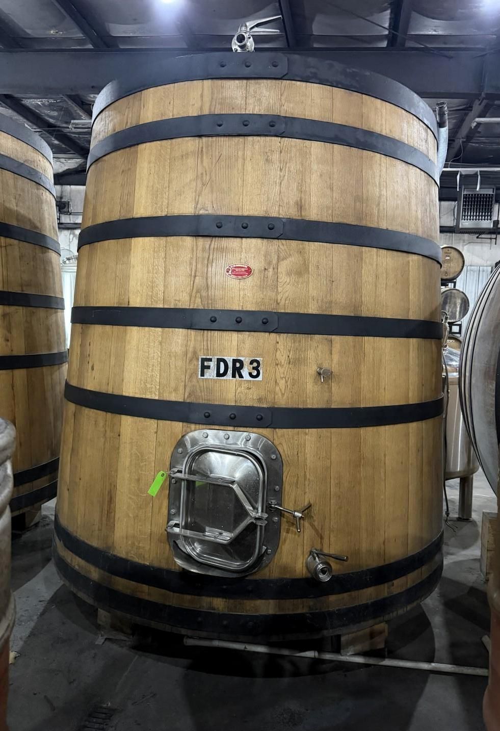 Large wooden fermentation tank with black bands and a metal hatch in an industrial room