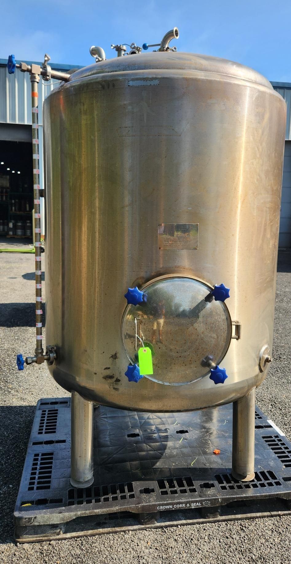 Stainless steel industrial tank outdoors on a metal platform, with pipes and fittings attached.