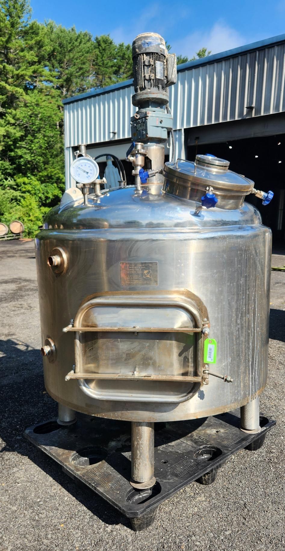 Stainless steel industrial mixing tank with motor on top, outdoors by a metal building