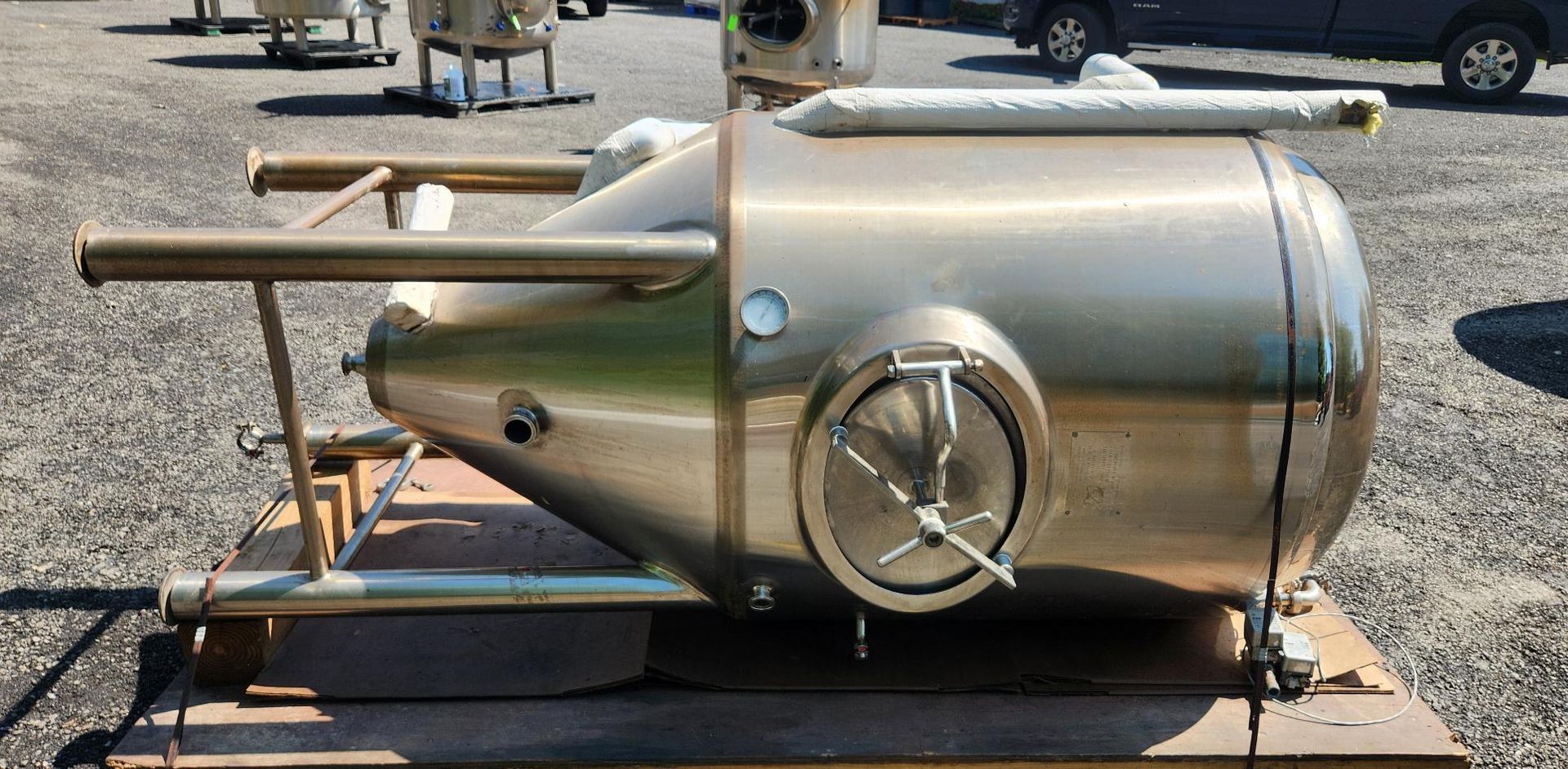 Polished stainless-steel cylindrical machine mounted on a pallet outdoors on gravel
