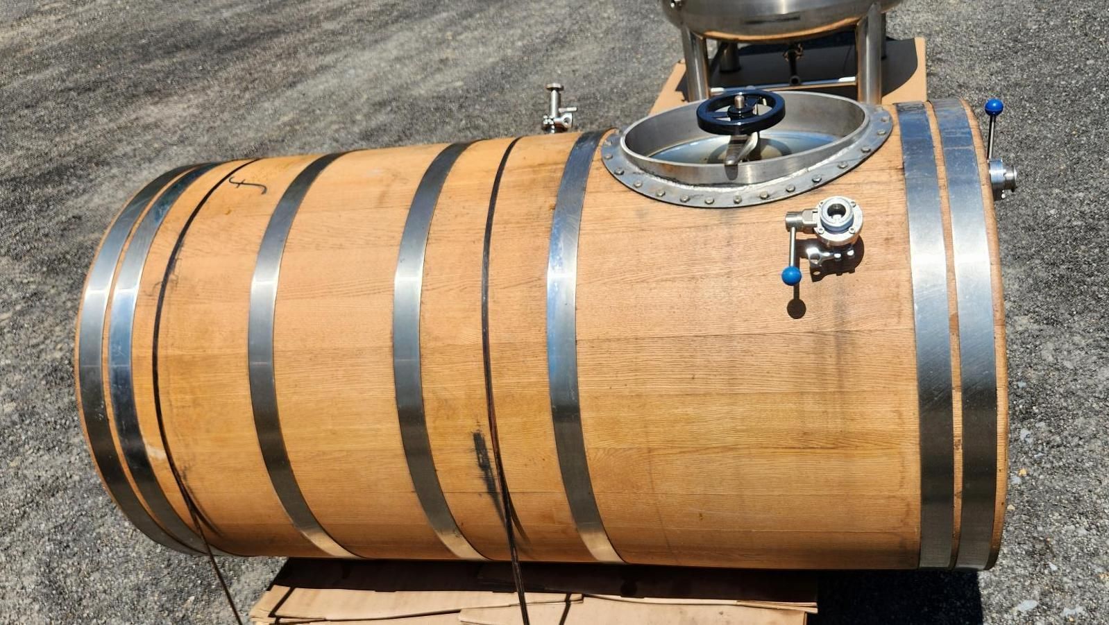 Oak whiskey barrel with metal bands and a spigot, sitting on a pallet outdoors.