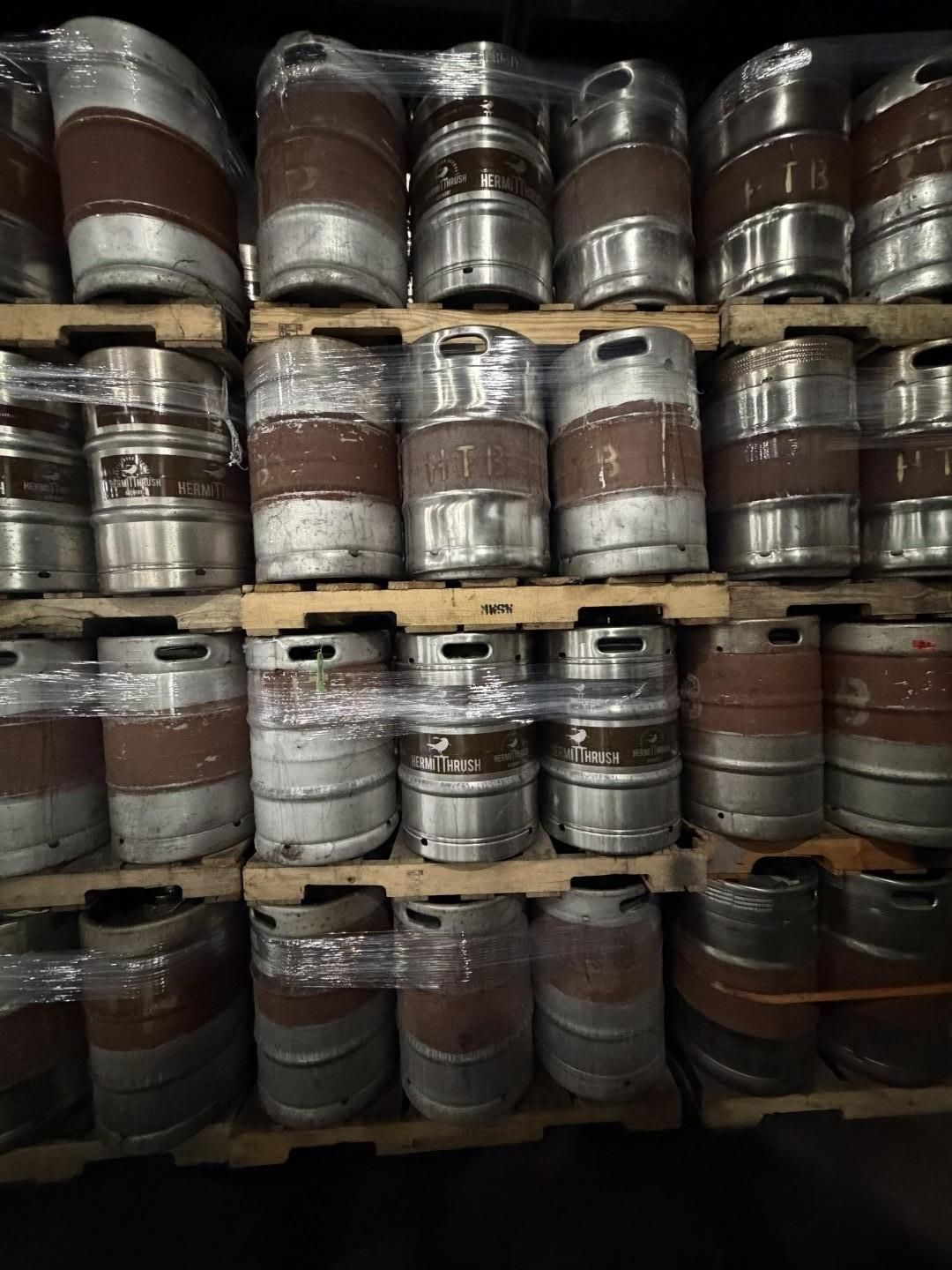 Stainless steel beer kegs stacked on wooden pallets in a warehouse.