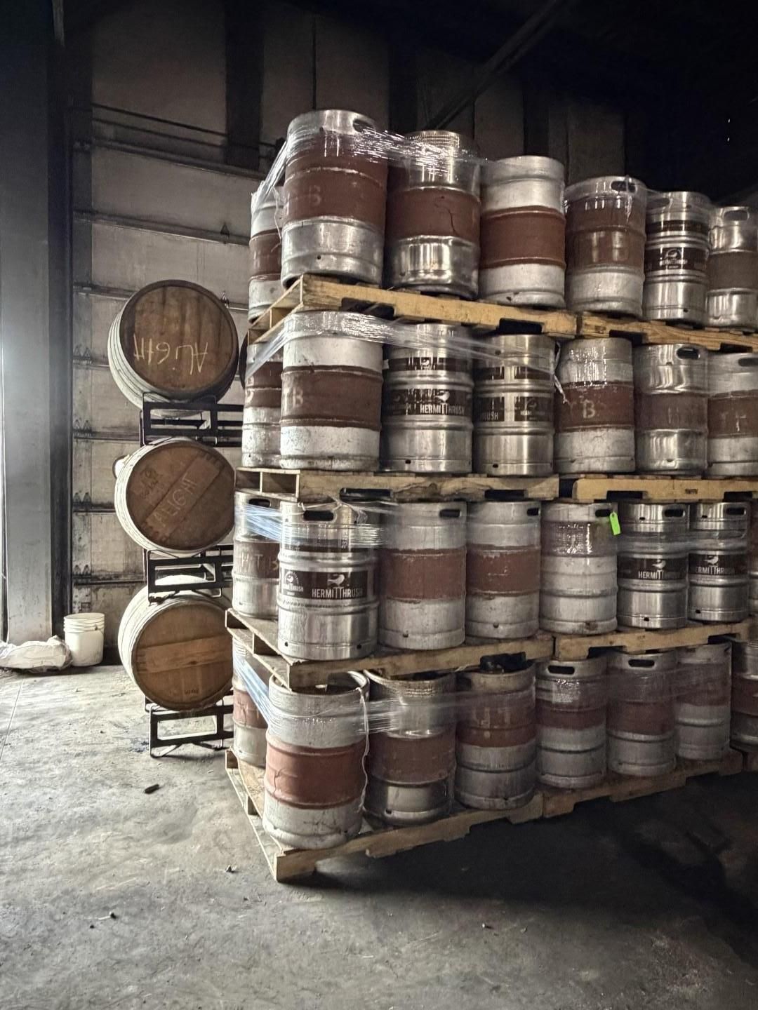 Stacked wooden barrels in a warehouse beside a wall and metal pallet rack