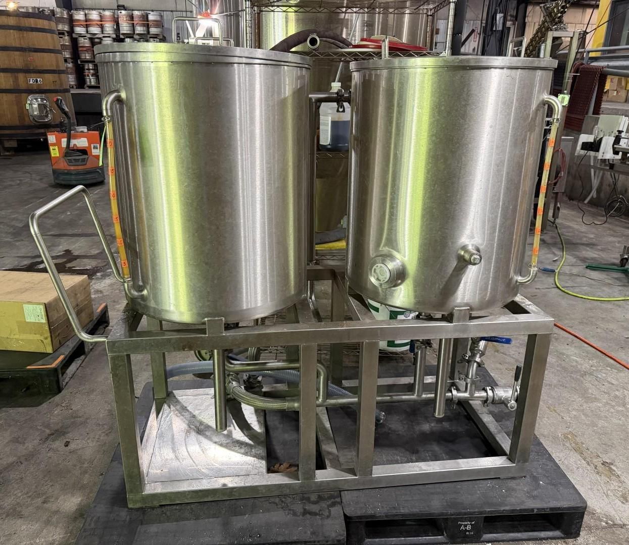 Two stainless steel industrial tanks on a metal frame in a warehouse setting