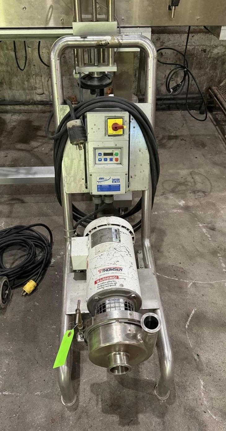 Industrial pump assembly with control box and pipes in a workshop, shown on a concrete floor.