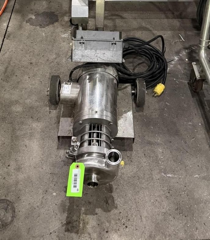Stainless steel industrial pump on a concrete floor with a green tag and coiled black cable nearby
