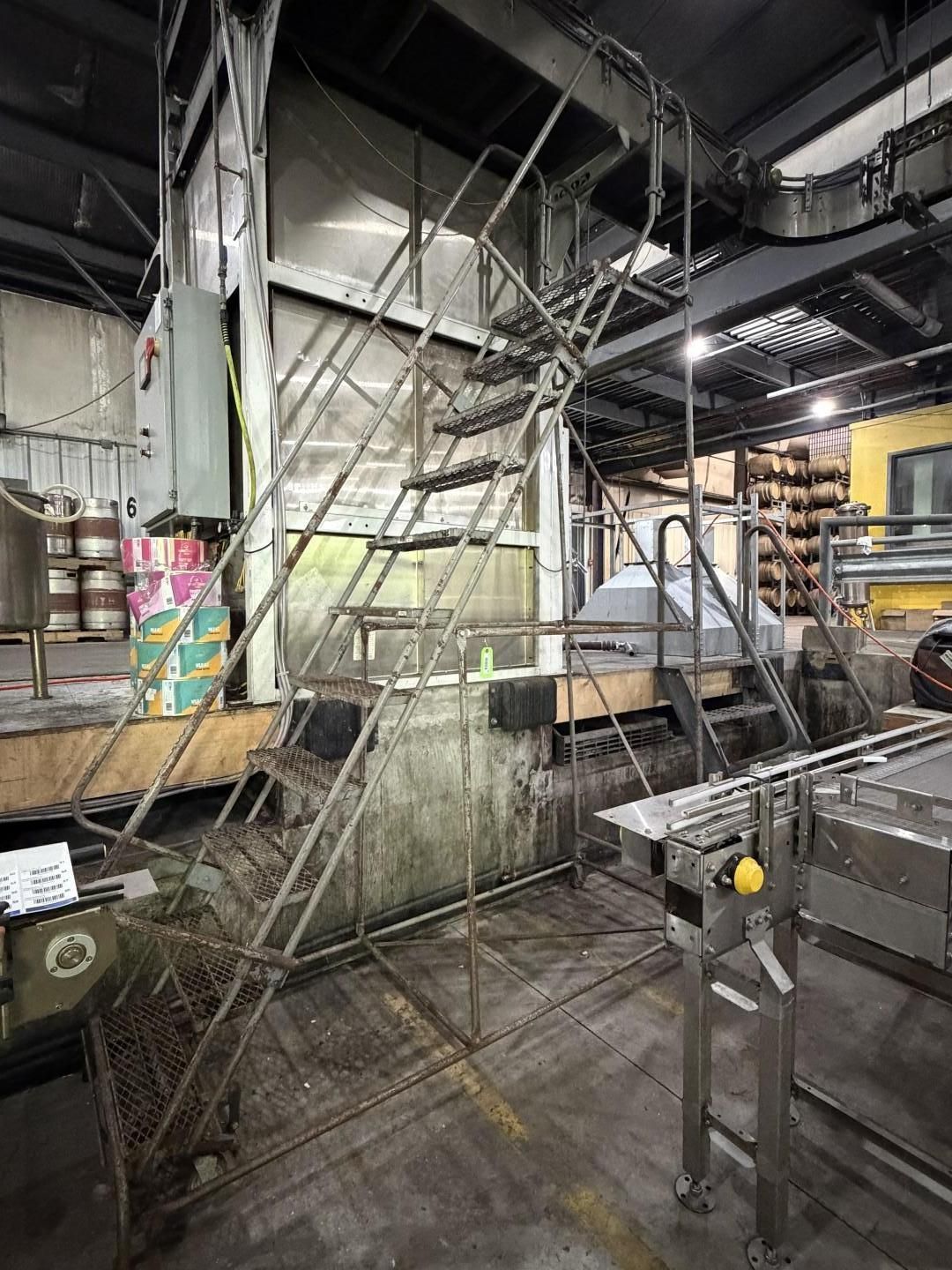 Industrial factory interior with metal stairs, tanks, pipes, and a work platform under bright lights