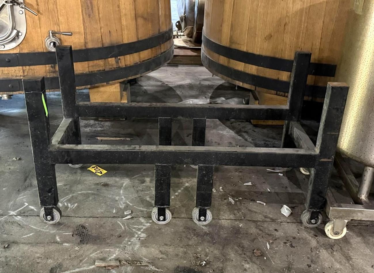 Black metal frame on casters beneath wooden barrels in a workshop-like setting