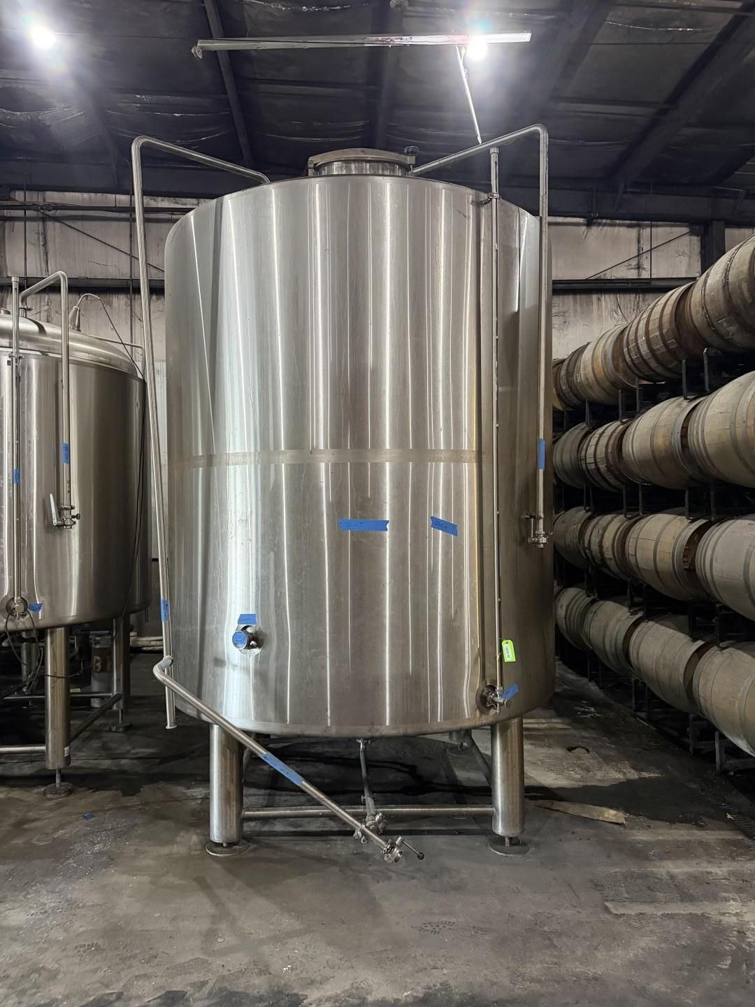 Large stainless steel industrial tank in a factory, with pipes and ductwork around it.