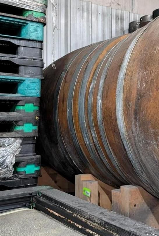 Large metal cylinder beside stacked industrial pallets in a warehouse.