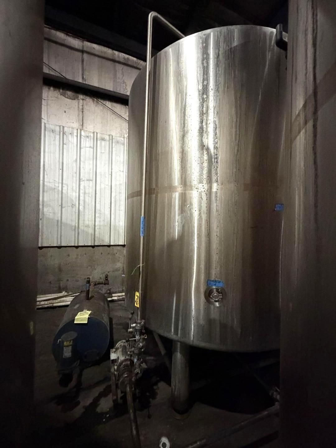 Large stainless steel tank in an industrial warehouse, with a worker inspecting equipment beside it.