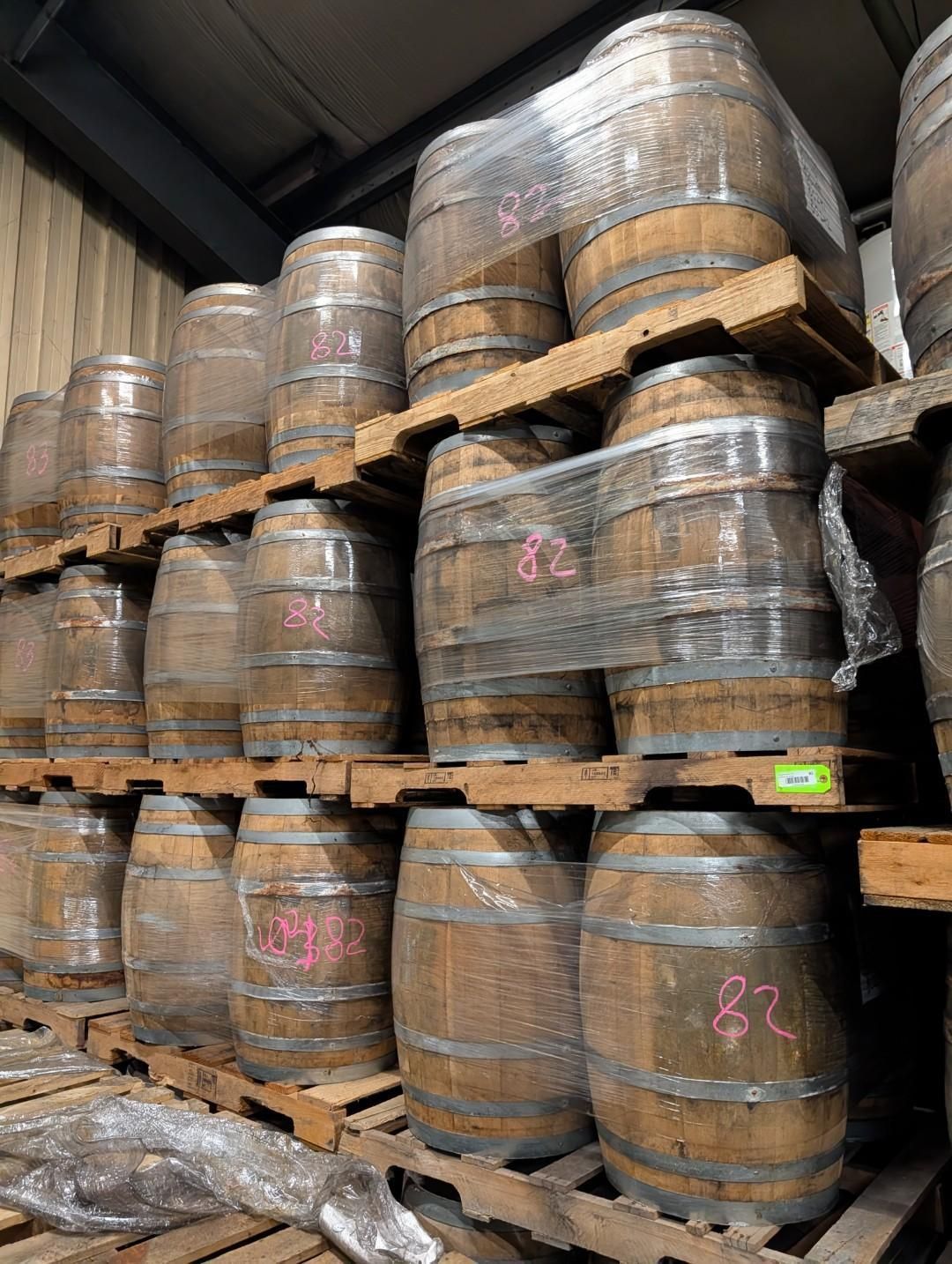 Rows of wooden barrels wrapped in plastic and strapped on pallets in a warehouse.