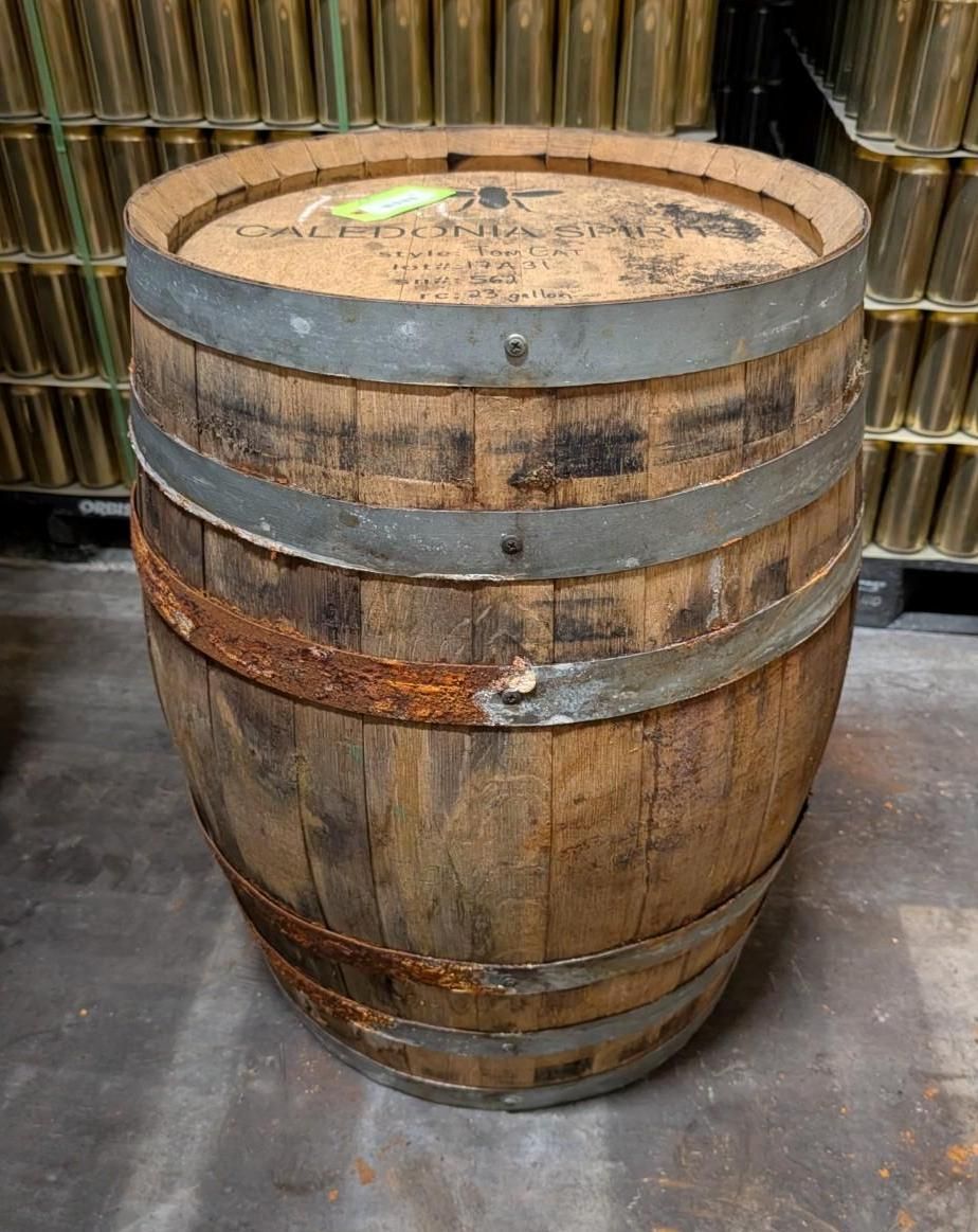 wooden barrel with metal bands standing indoors on a concrete floor.