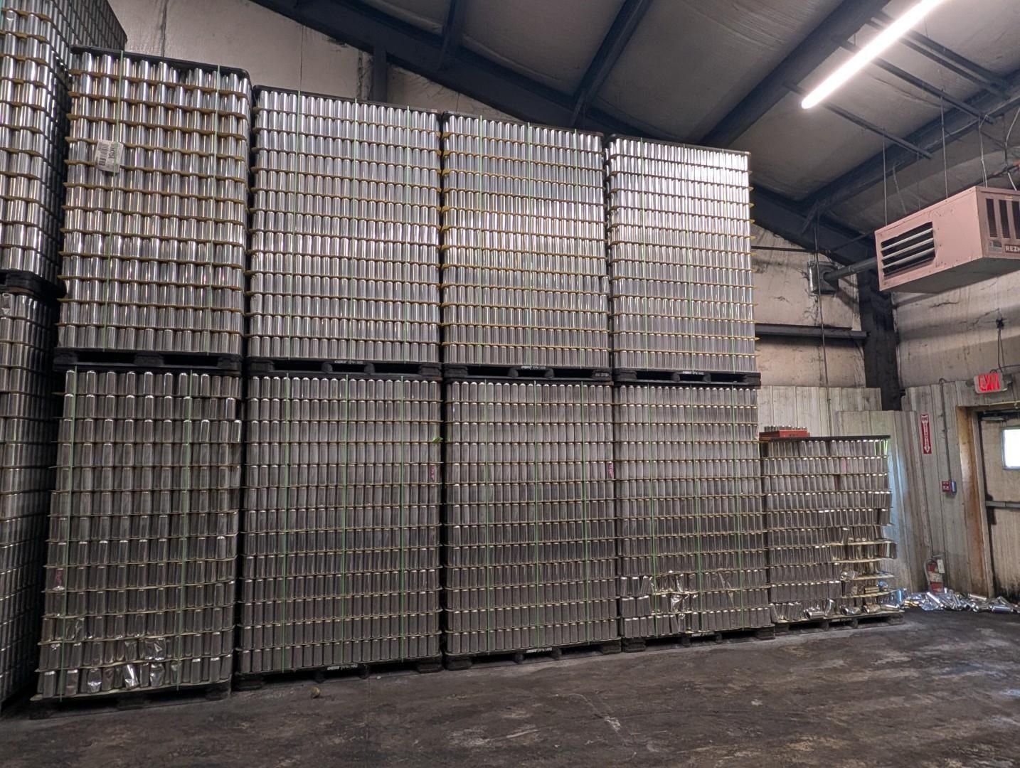 Stacks of metal cans piled high inside an industrial warehouse.